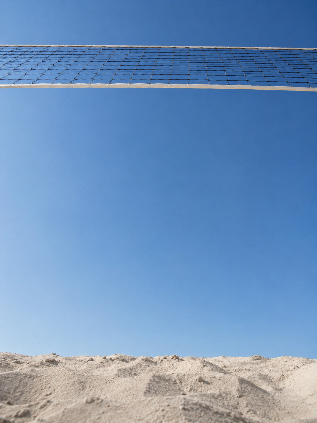 Ein Volleyballnetz über Sand an einem klaren blauen Himmel.