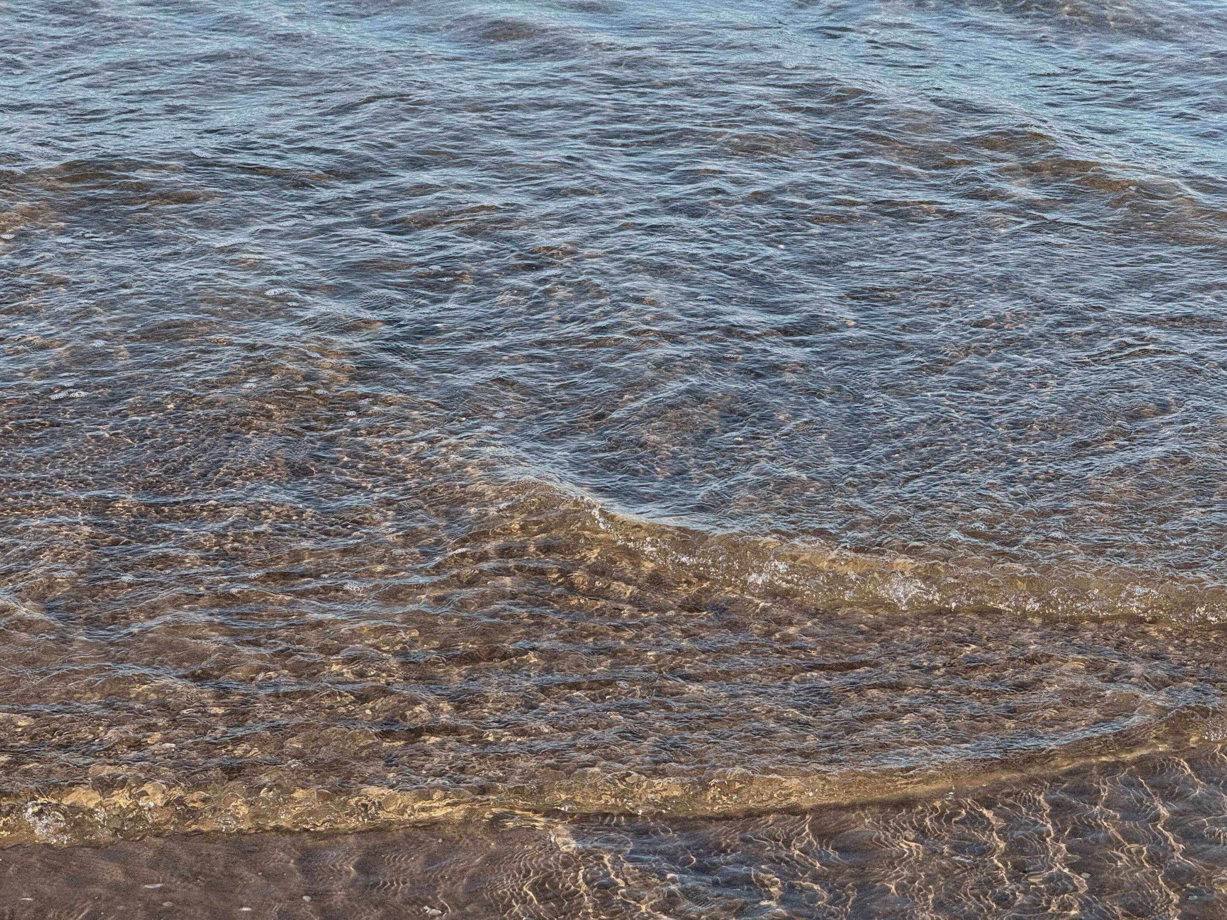 Klares Wasser, das an einen Steinstrand gespült wird.