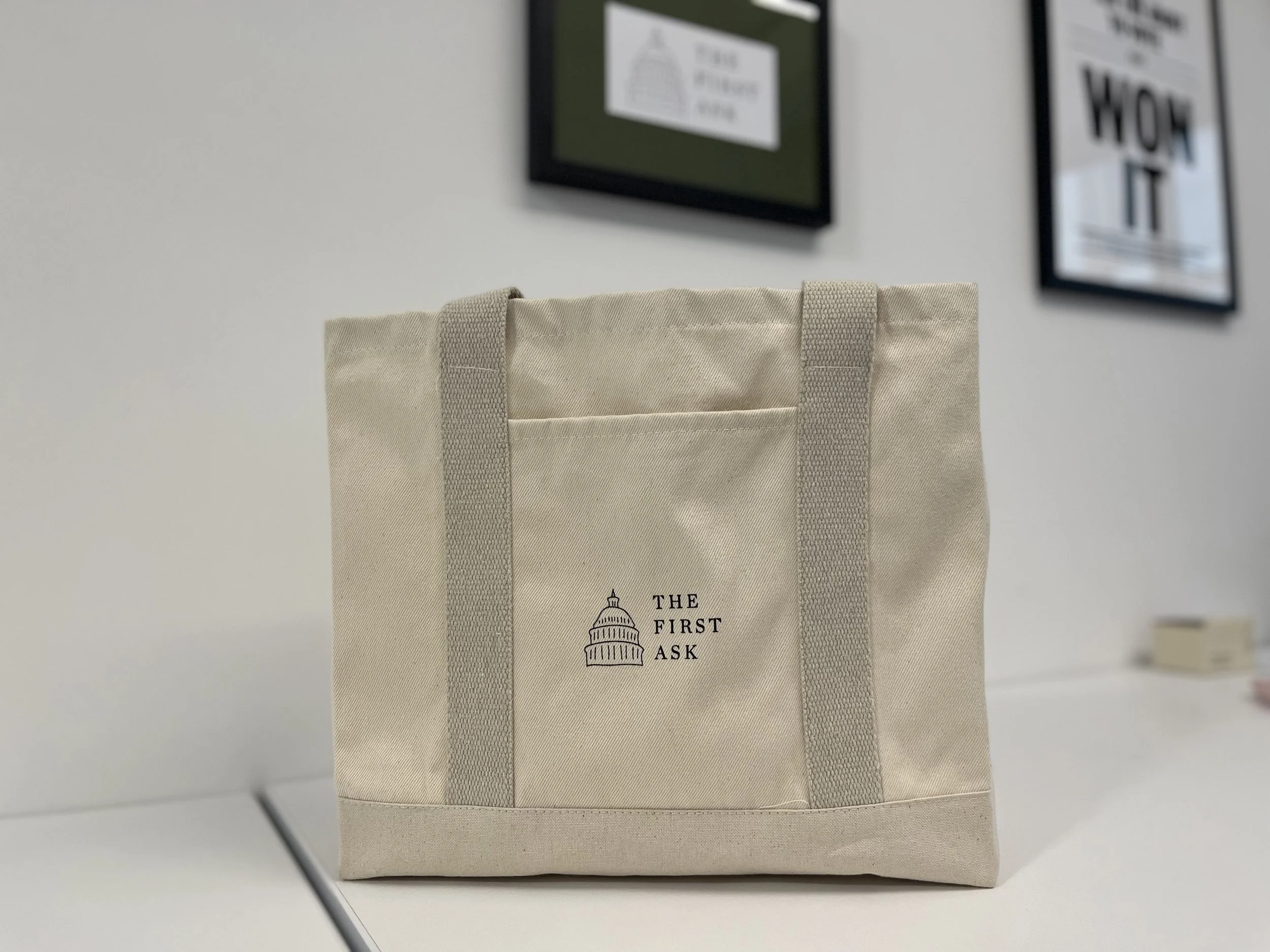 The First Ask Tote - Light beige square canvas tote bag with one outer pocket. A small First Ask capitol logo is on the outer pocket.