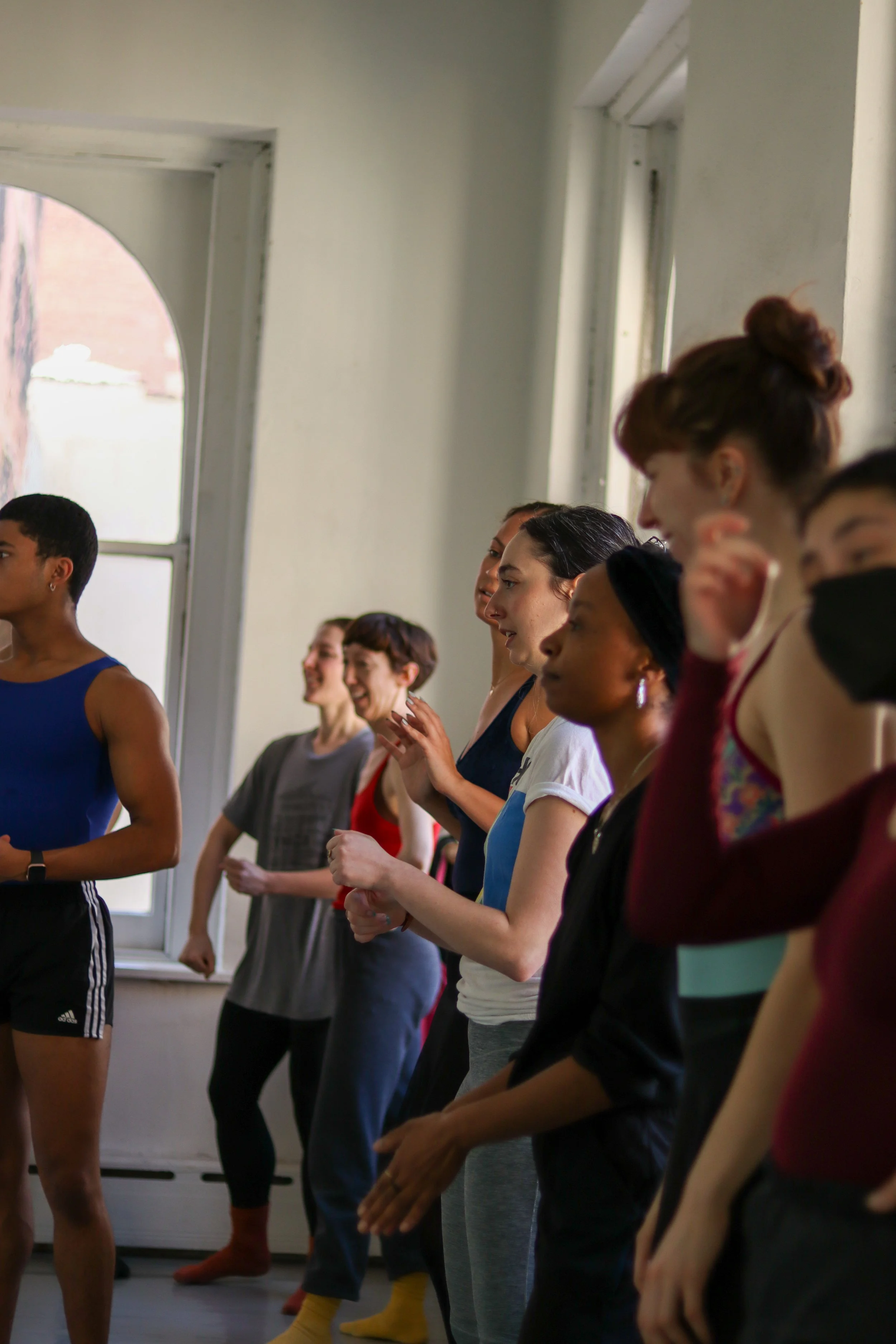 Group of diverse women and men standing in a dance studio, practicing ballet or modern dance, with some smiling and focused.