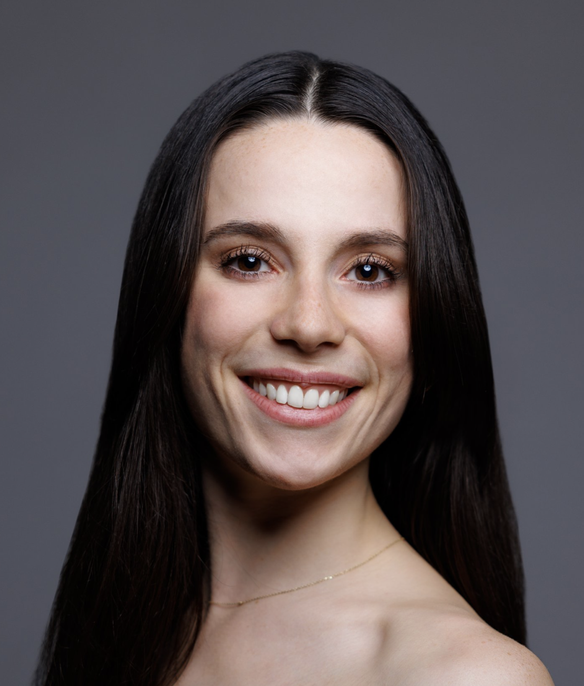 Close-up portrait of a woman with long dark hair, smiling against a gray background.