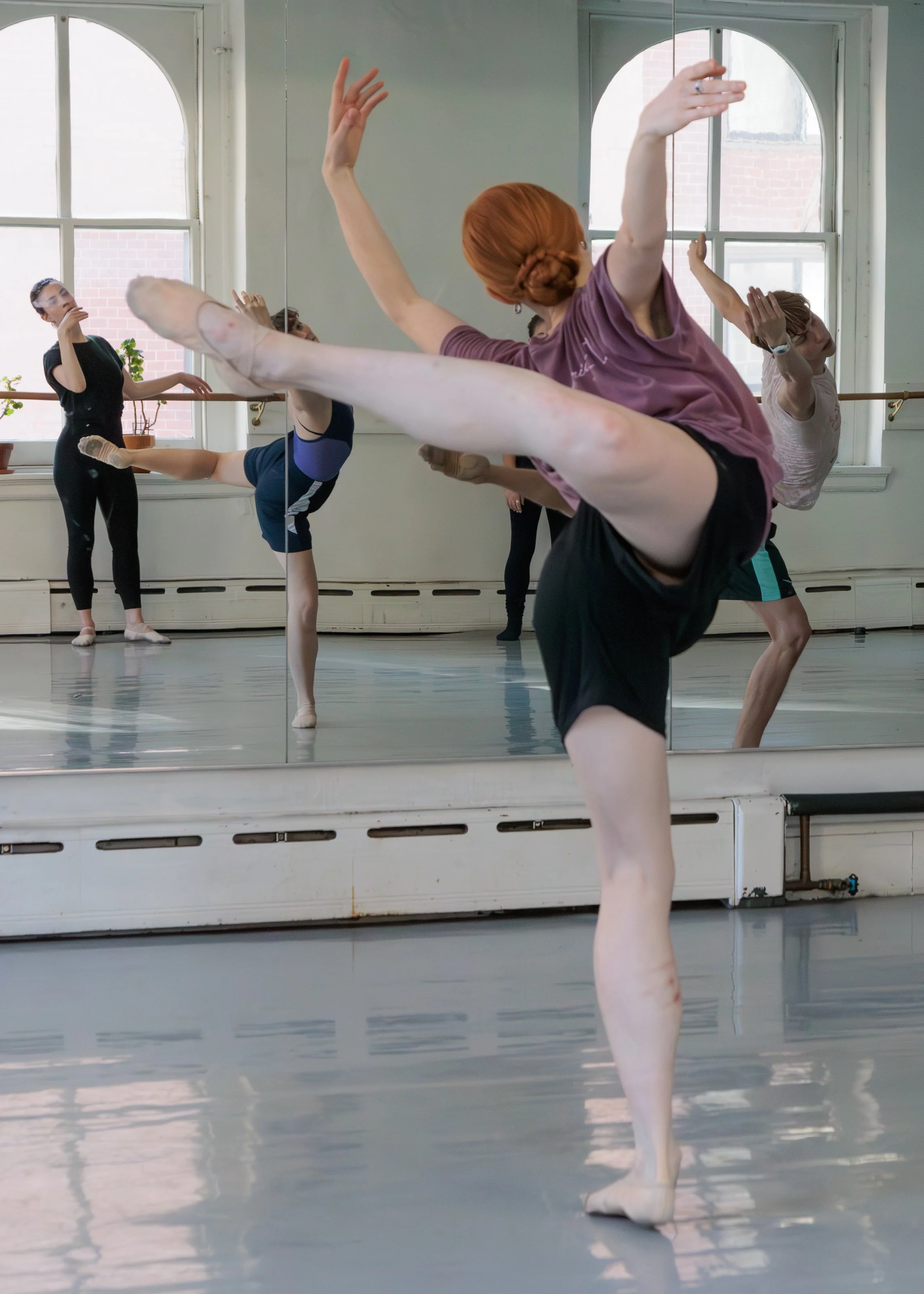Ballet dancers practicing in a dance studio, with three dancers performing a move while another watches.