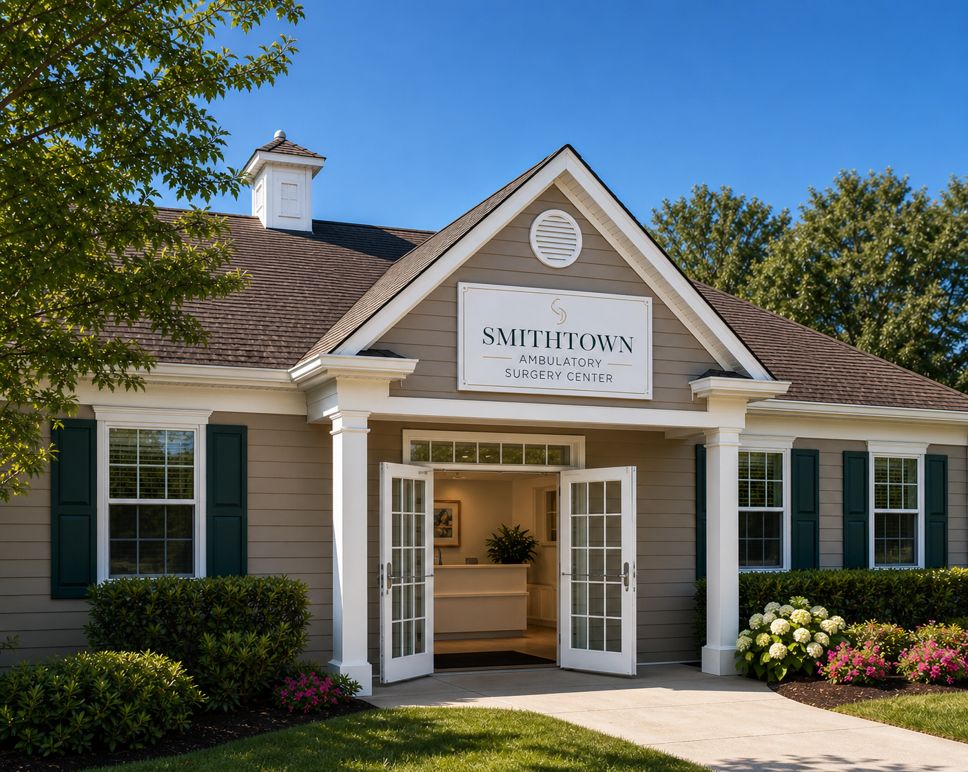 Exterior of a beige building with green shutters and a sign that reads 'SMITHTOWN AMBULATORY SURGERY CENTER.' Double glass doors are open, revealing a reception area with a potted plant.
