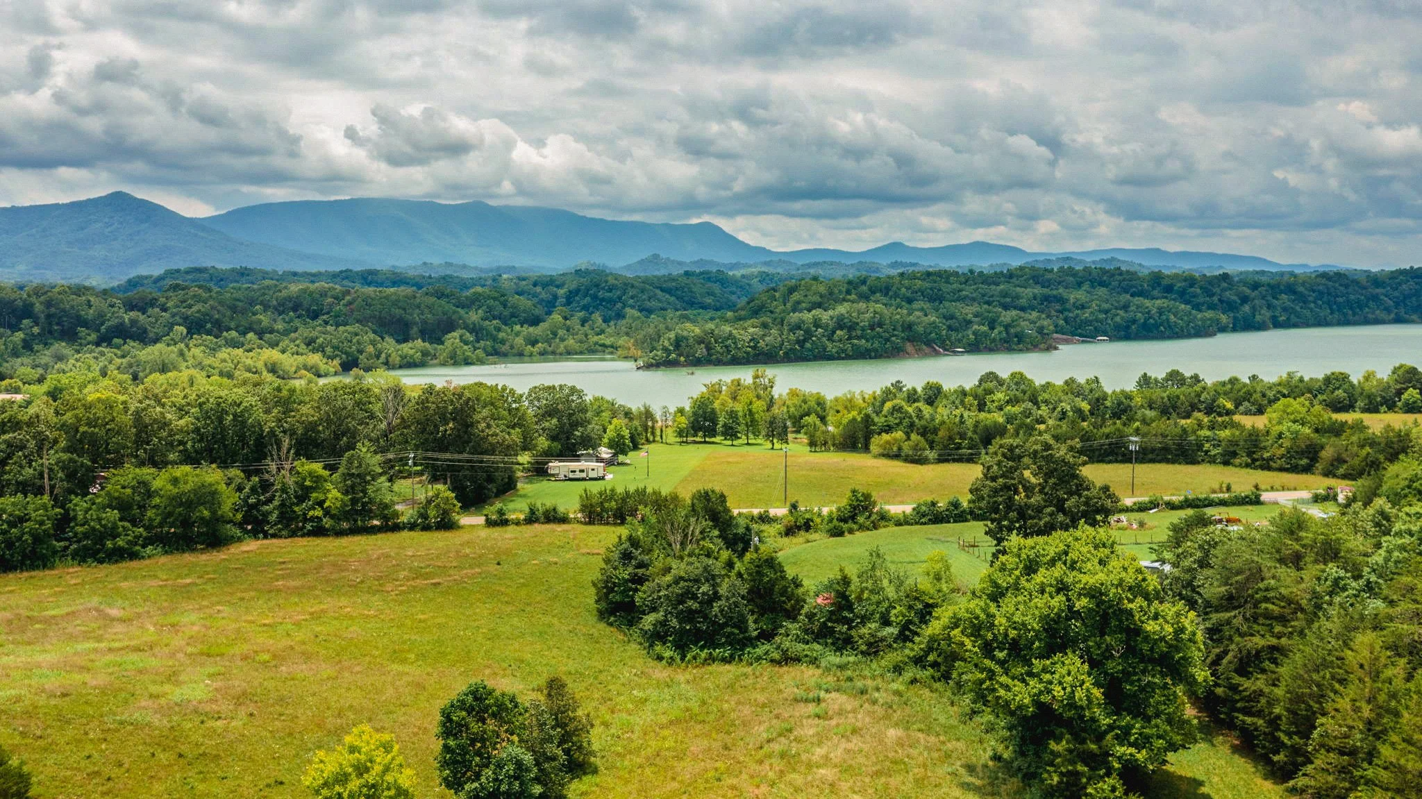 Scenic landscape of green trees, a river, distant mountains, and a cloudy sky.