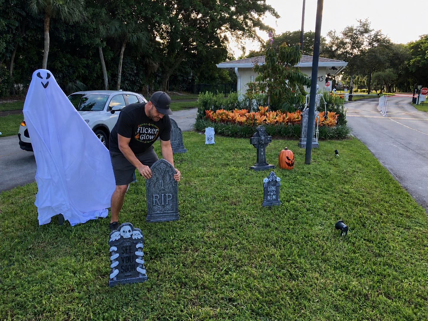 Person setting up Halloween decorations in front yard with tombstones, a ghost figure, and a carved pumpkin