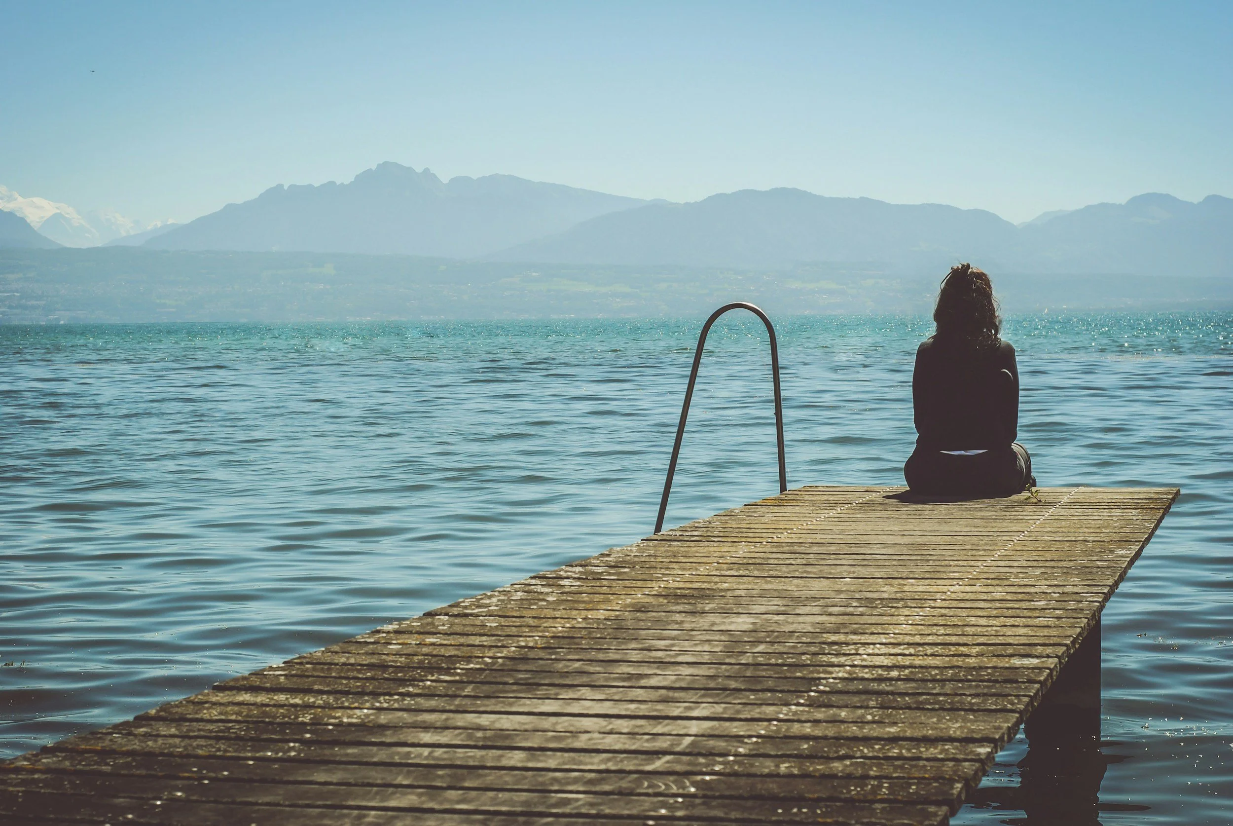 A person sitting at the end a dock on a lake.