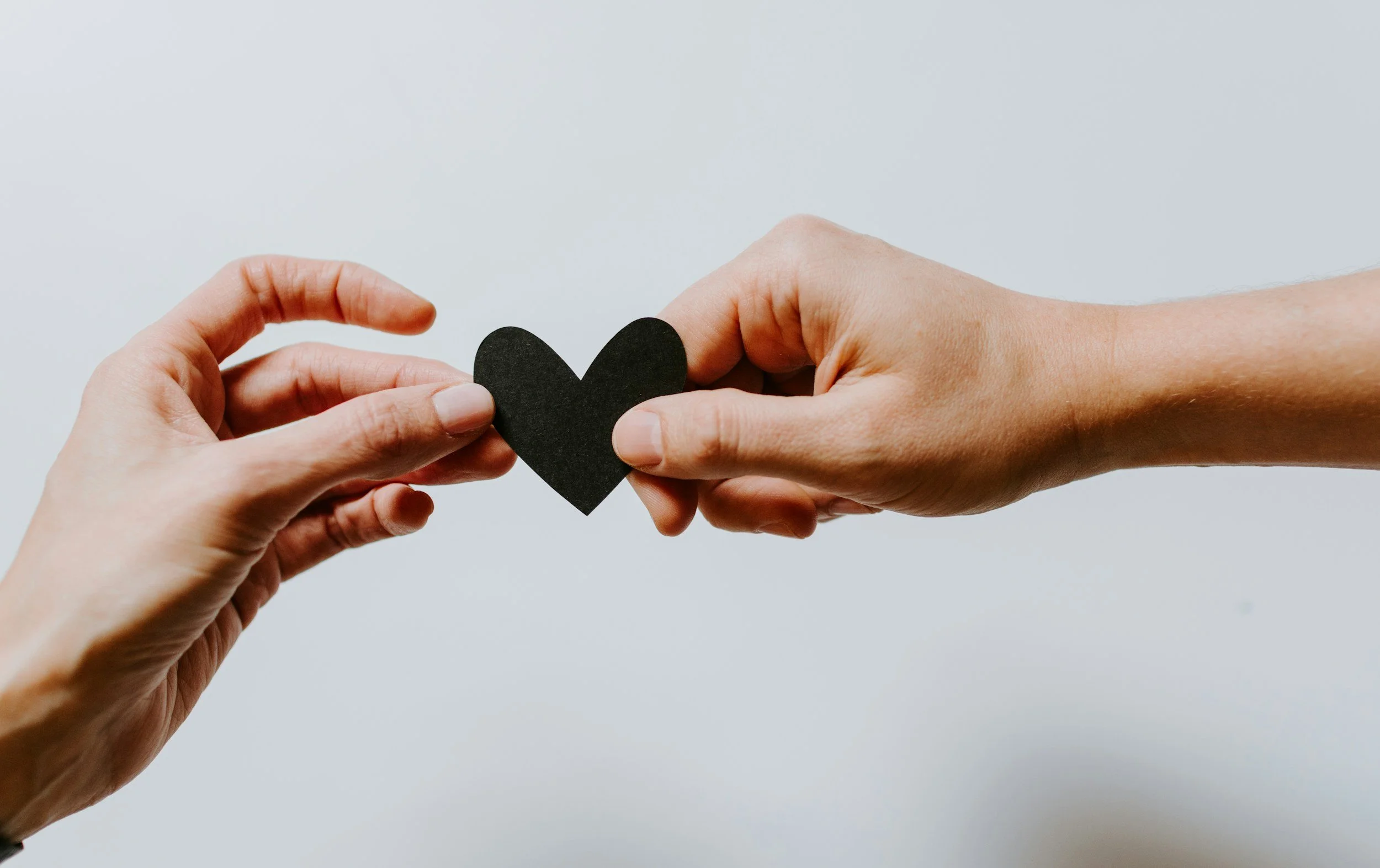Two hands exchanging a small black heart-shaped object.