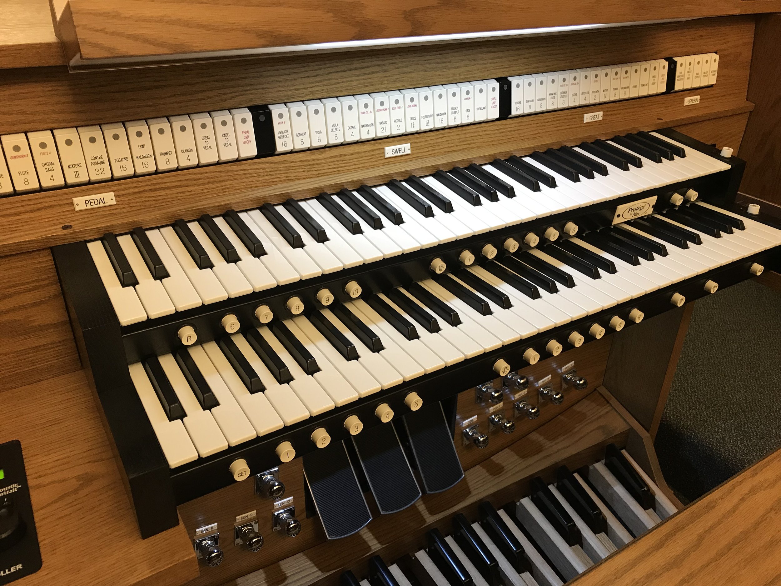 Close-up of a wooden electronic pipe organ keyboard with multiple rows of keys and labeled stops and controls.