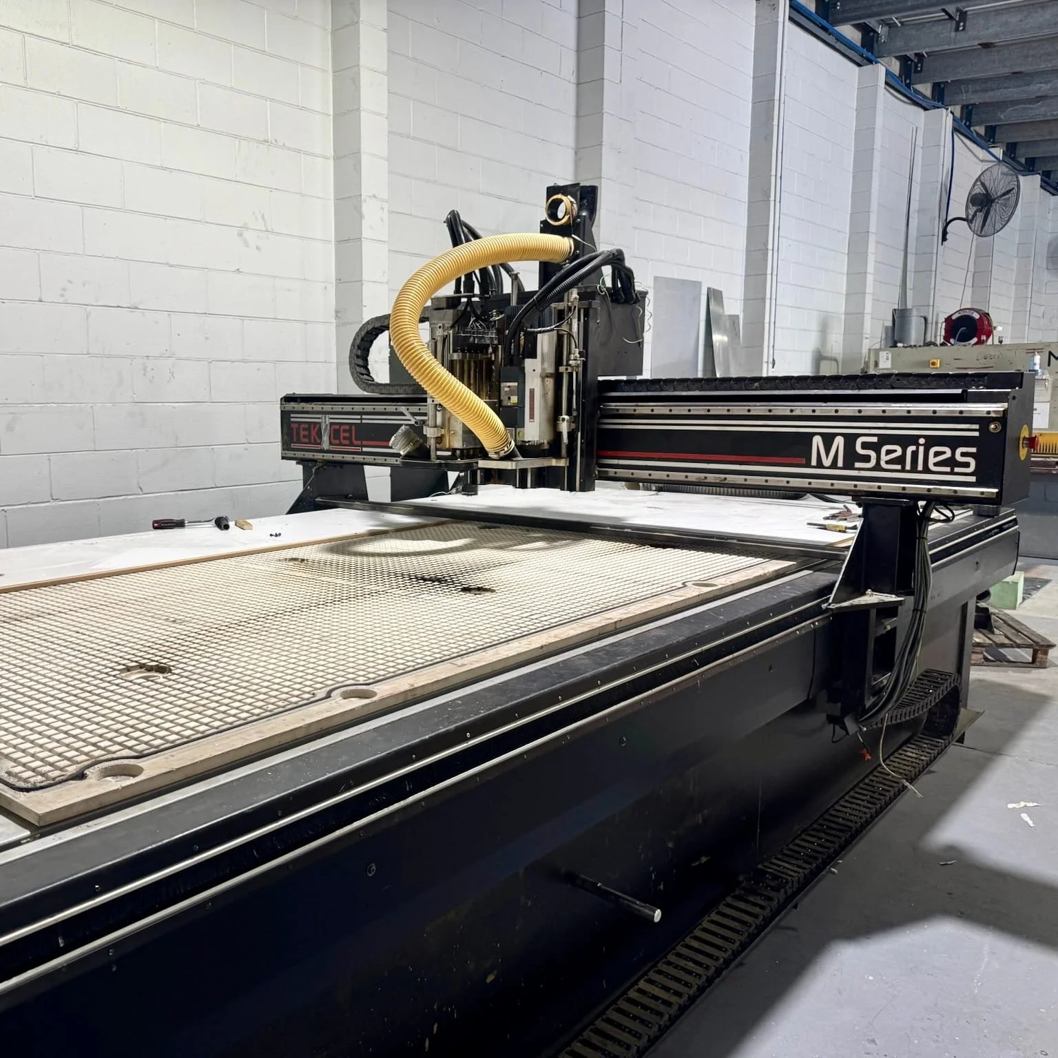 Large CNC machine in a workshop with a white brick wall background.