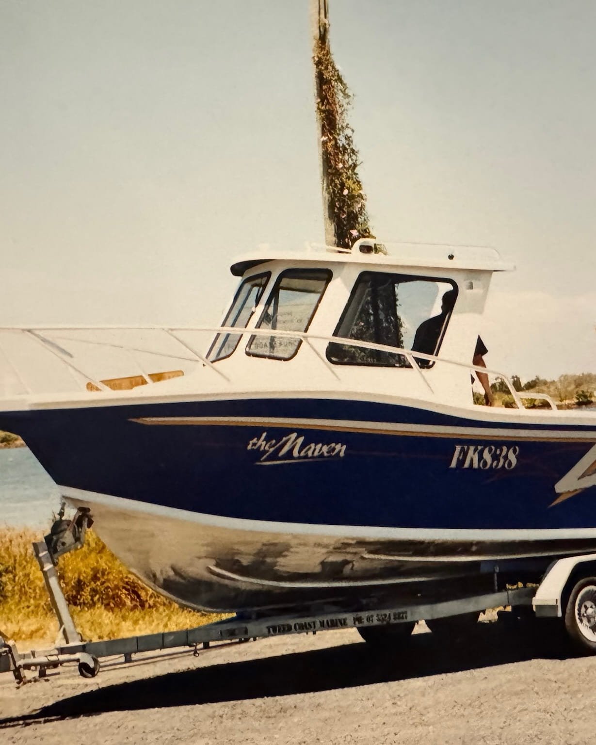 A blue and white boat named 'the Maven' on a trailer.