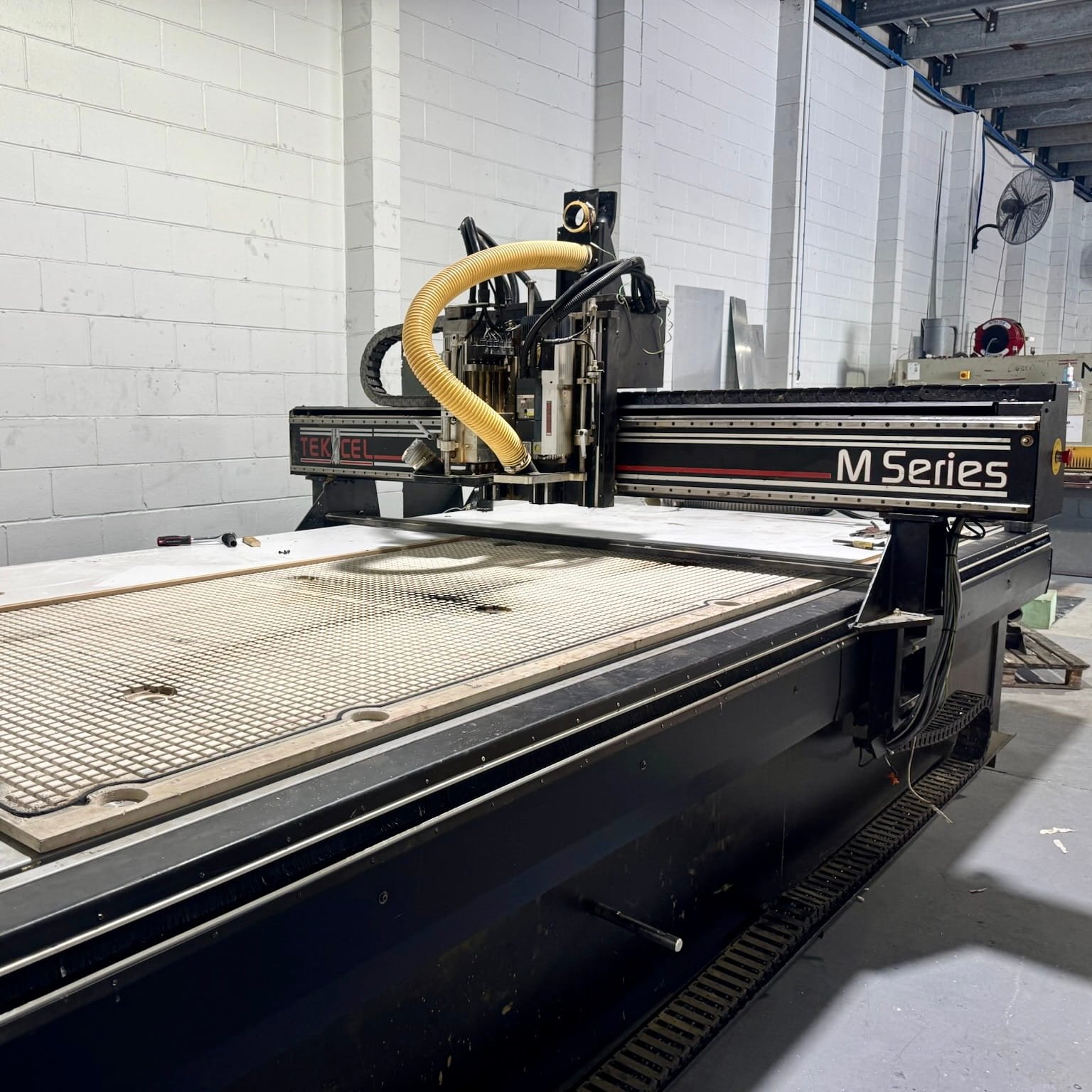 Large CNC machine in a workshop with a white brick wall background.