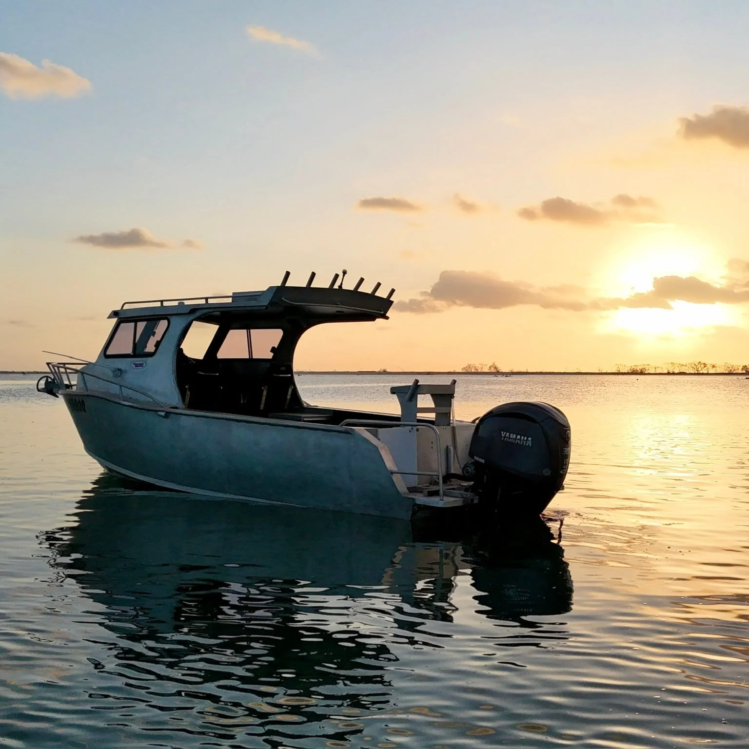 A boat floating on a calm body of water during sunset or sunrise, with a partly cloudy sky in the background.