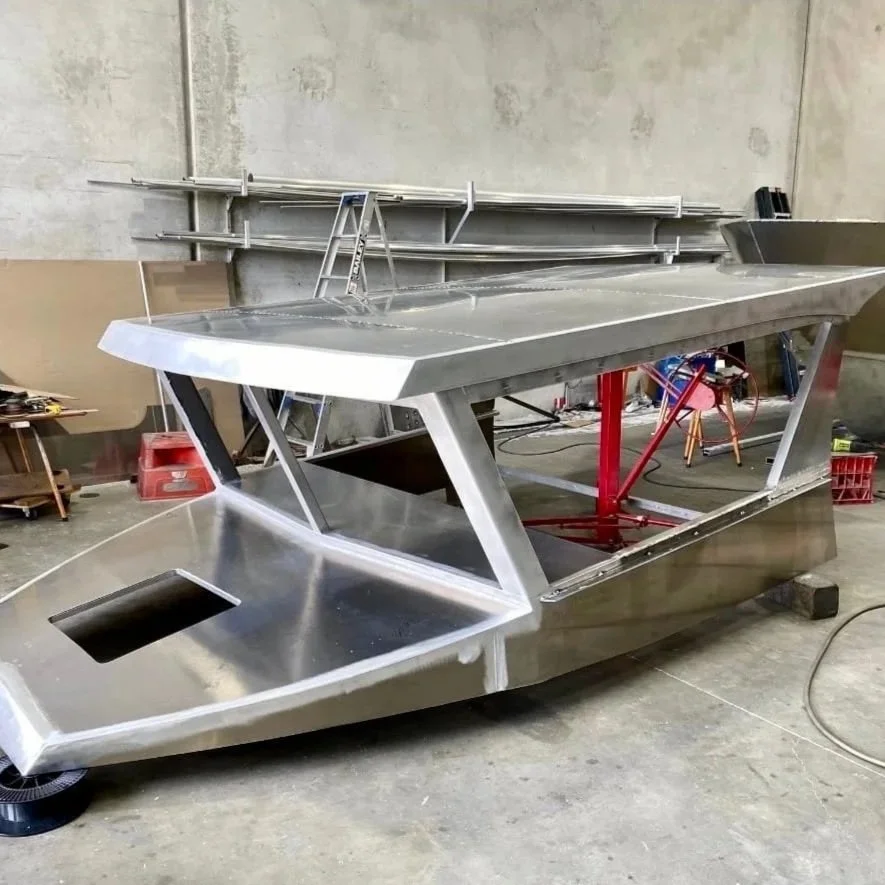 A metallic, boat-shaped frame or structure with angular design elements, located in a workshop or industrial setting.