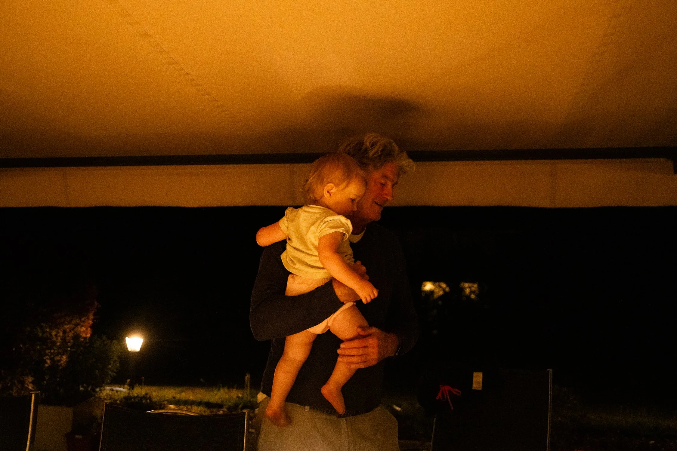 A man lifting a young girl in the air outdoors at night, with dim lighting and trees in the background.