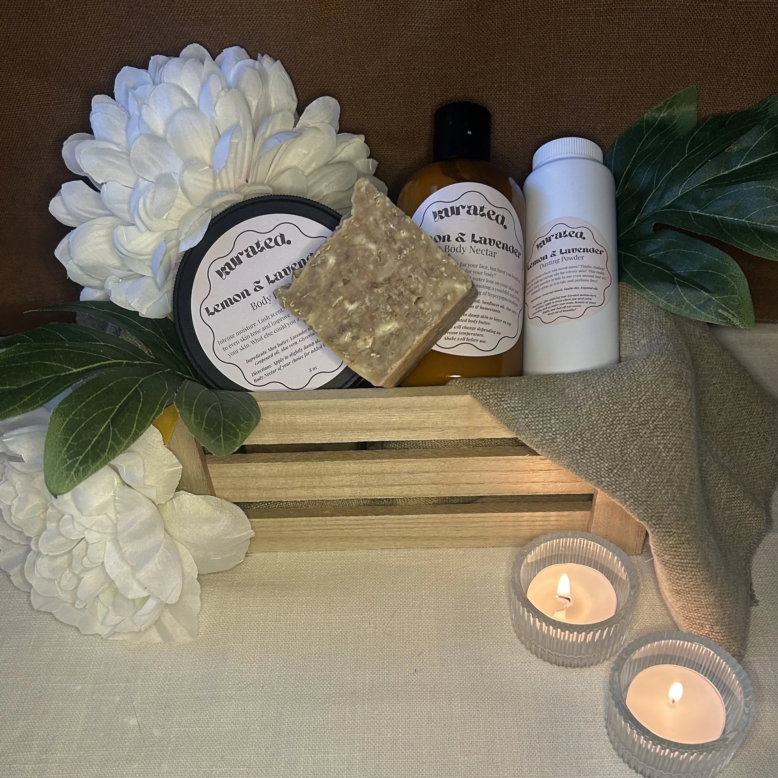 A floral arrangement with white flowers, green leaves, and candles on a beige cloth surface, with various bath and body products labeled 'Lemon & Lavender'.