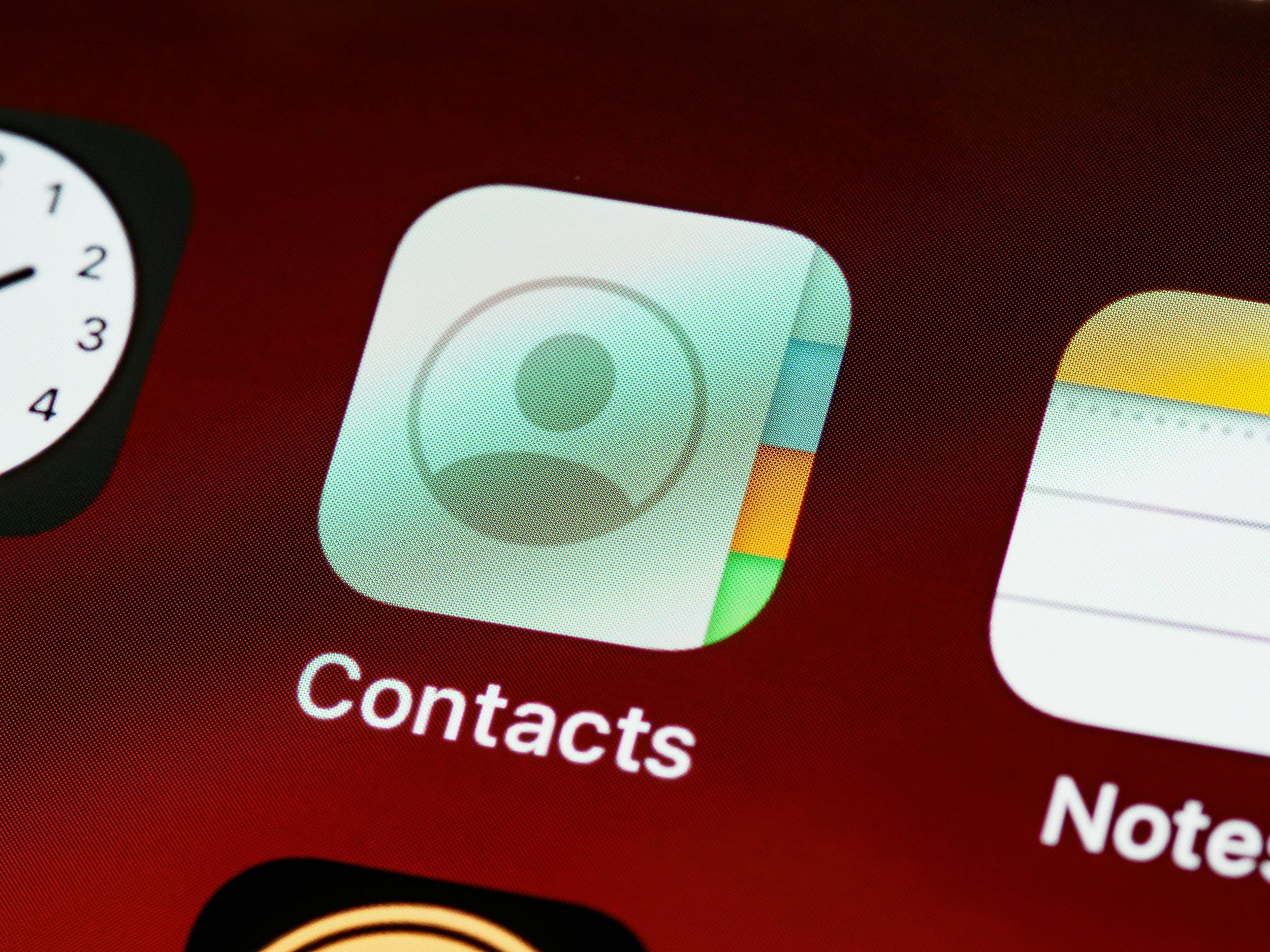 Close-up of a smartphone screen showing a contact list with the label 'Contacts' at the bottom and app icons including Calendar, Mail, and Notes partially visible.