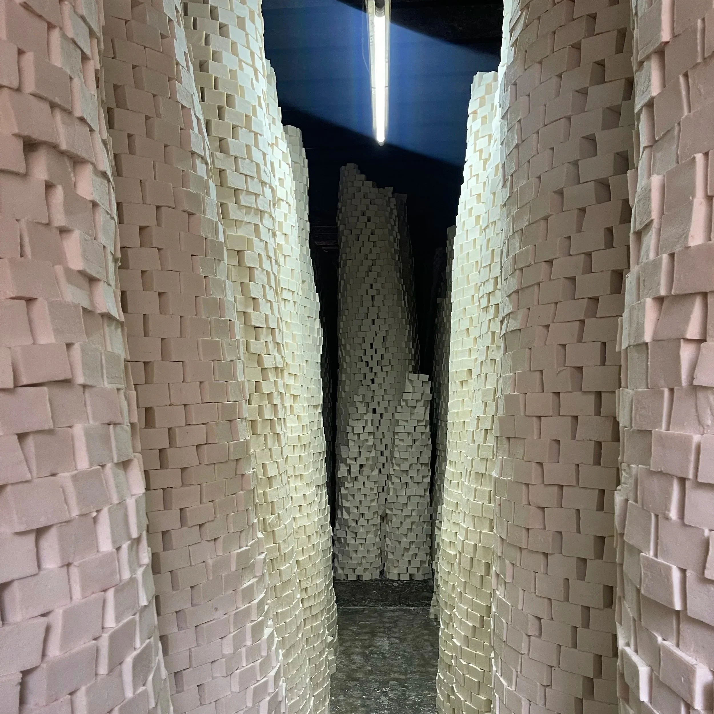 A narrow corridor lined with tall, curved brick walls, illuminated by a fluorescent light fixture on the ceiling.
Drying towers of Al-Jamal Nabulsi Olive Oil Soap.