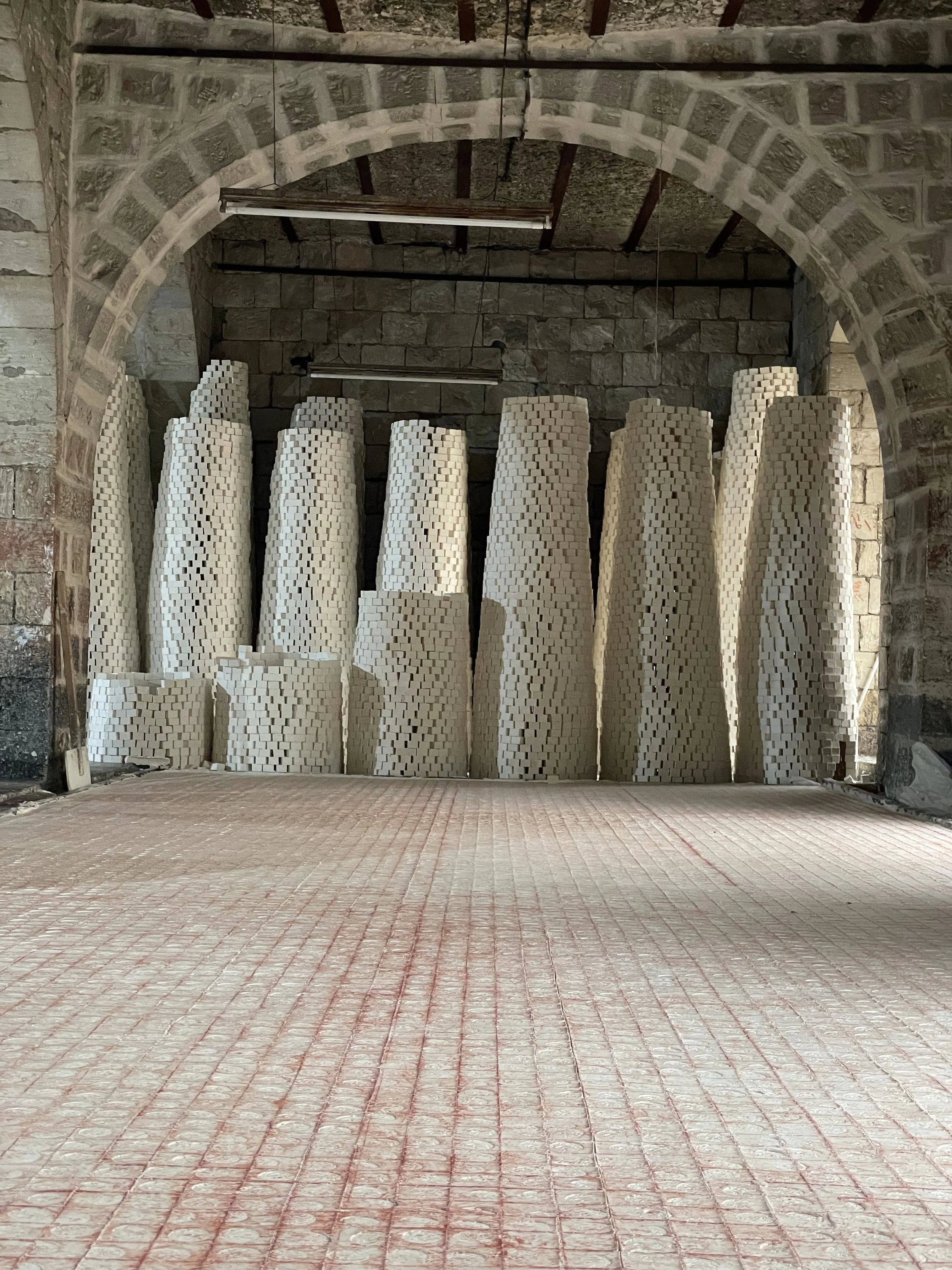 Interior view of a hall with an arched brick ceiling and stone walls, where a row of white sculptural columns made of Al-Jamal Nabulsi Olive Oil Soap Bars.