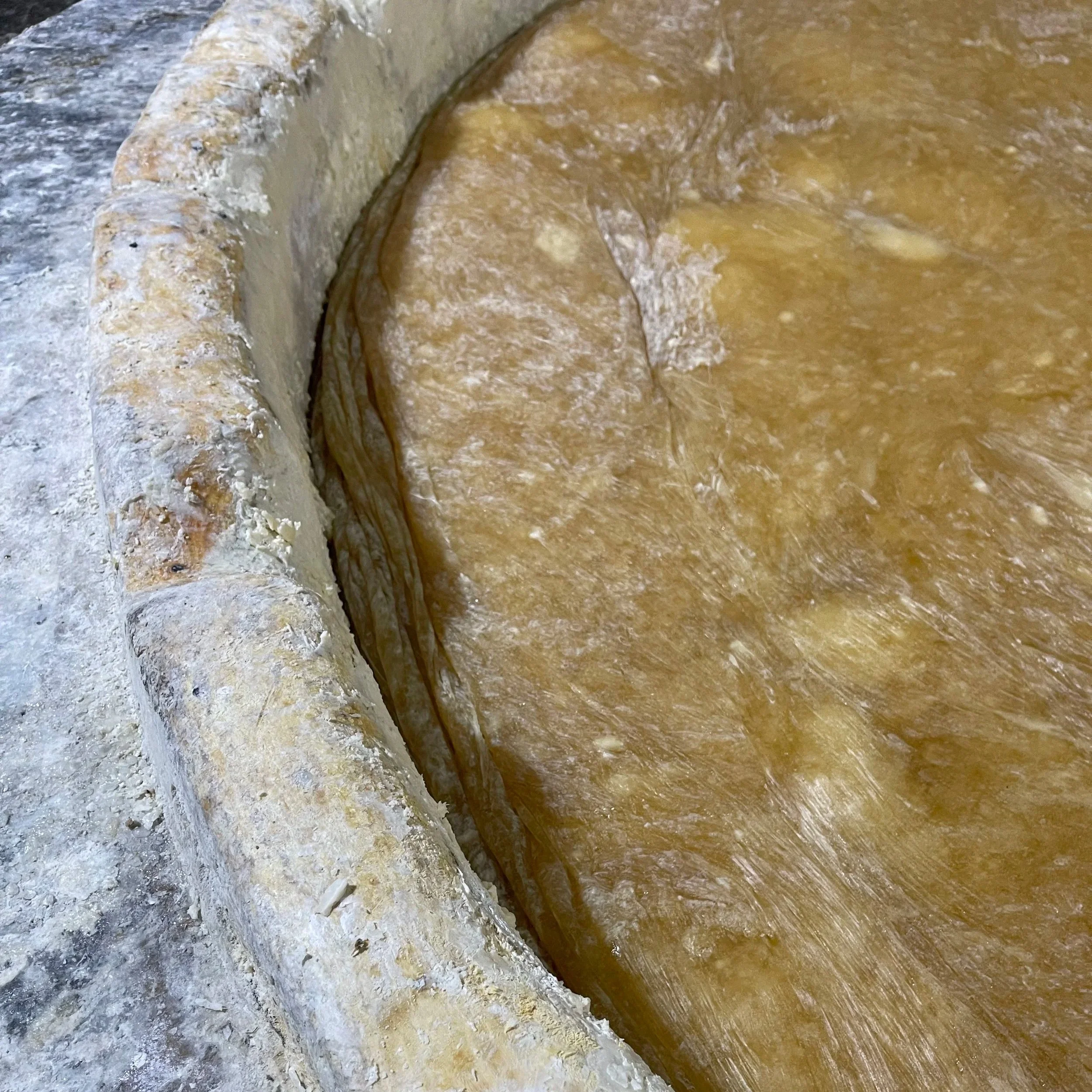 Close-up of a textured, curved detail on a stone or concrete surface with different colors and textures, including gray, white, and yellowish-brown areas.
Cooking process of Al-Jamal Nabulsi Olive Oil Soap.