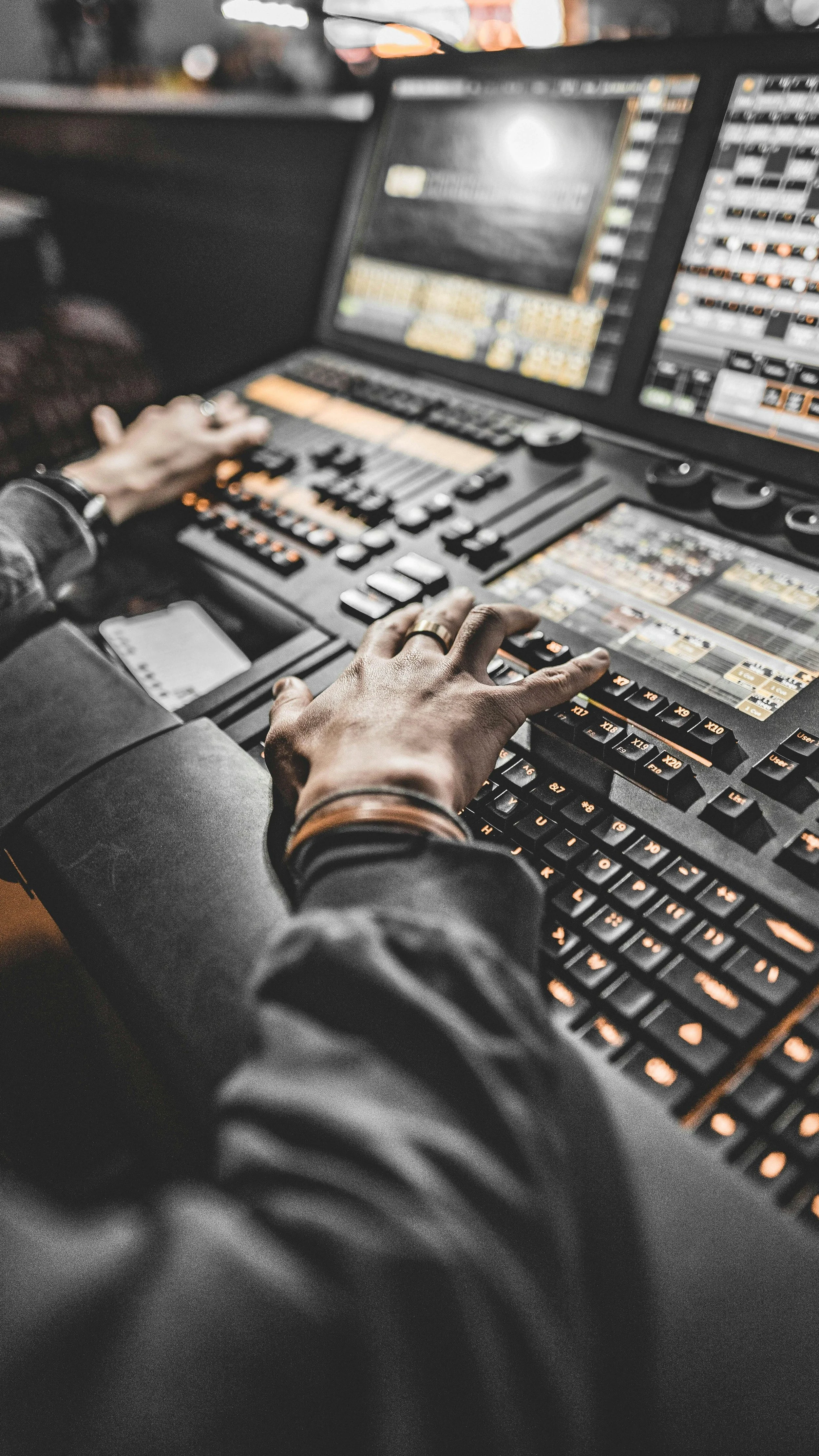 A person's hands operating a professional DJ or music production mixing console with multiple screens and controls.