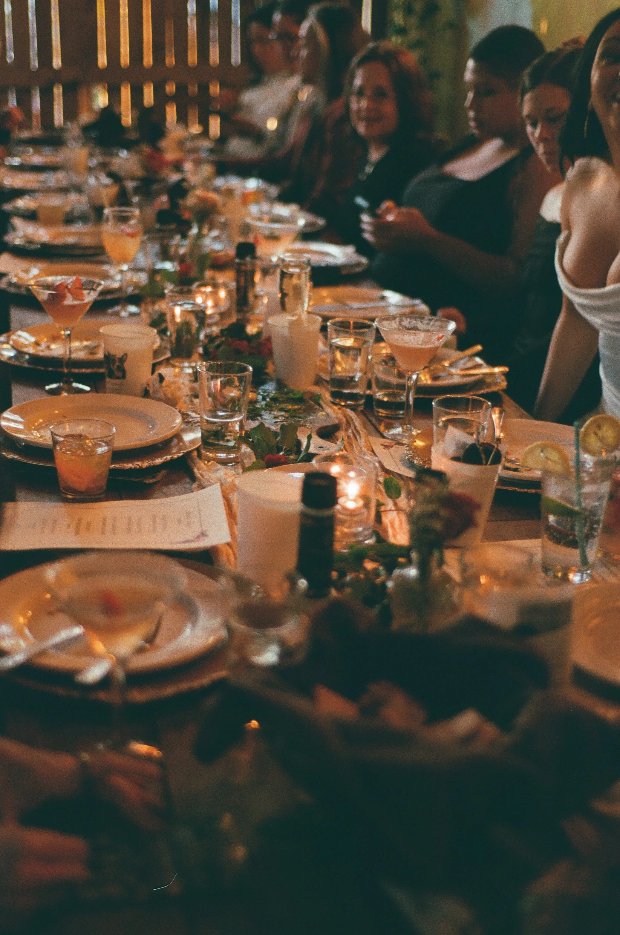 A group of people seated at a long table during a dinner event, with plates, glasses, and drinks.