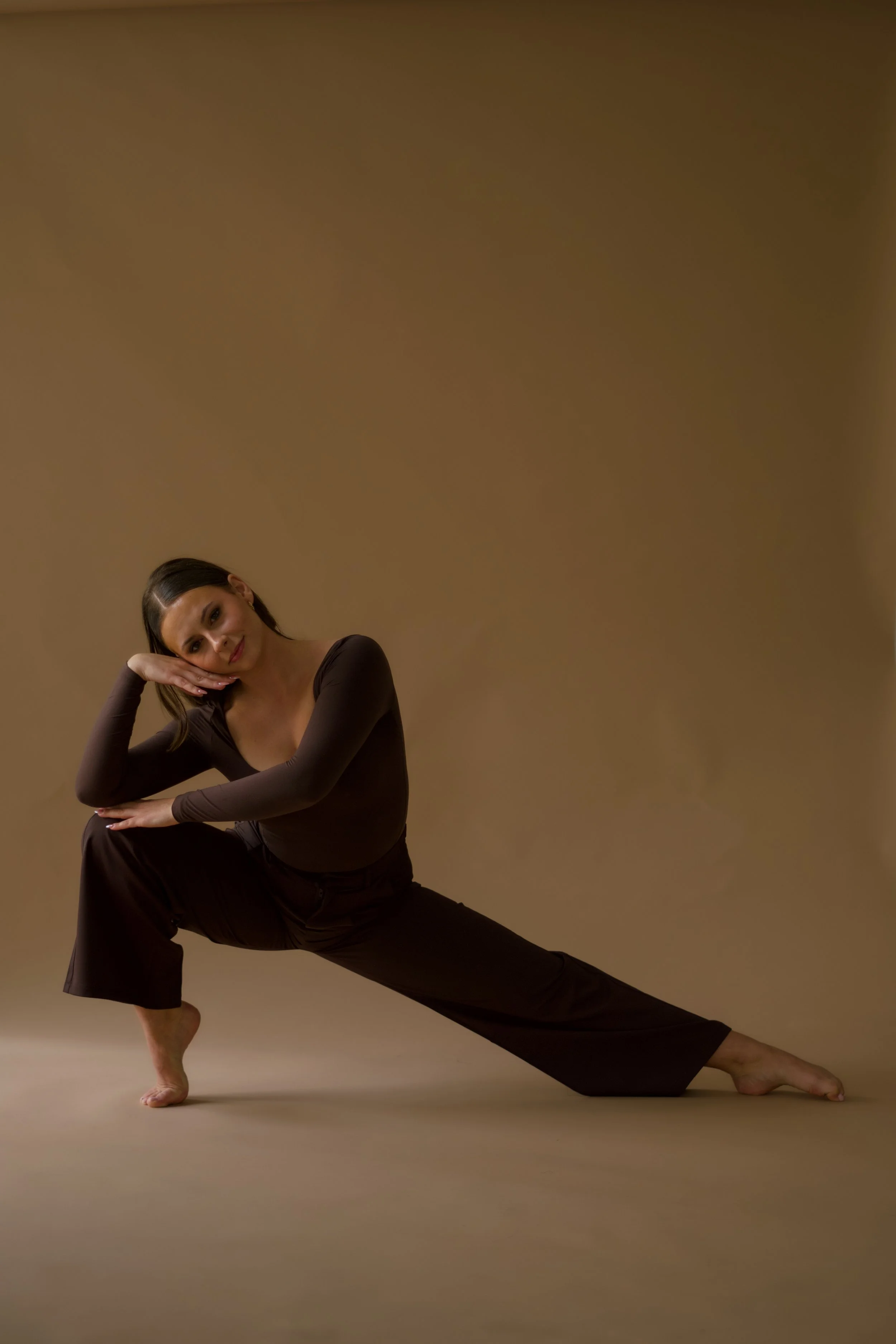 A woman in a black outfit performing a yoga pose against a plain brown background.