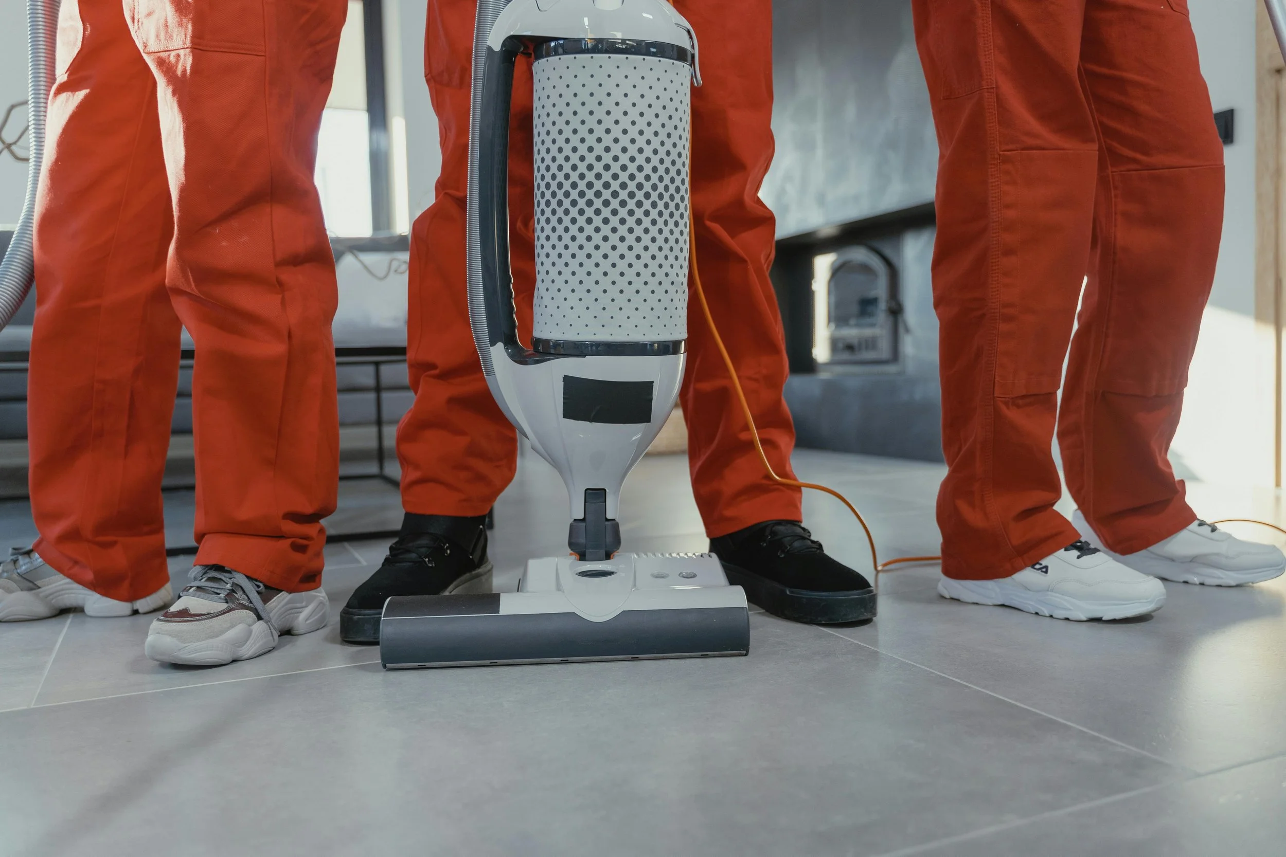Three people in orange uniforms using a floor cleaning robot in a tiled room.