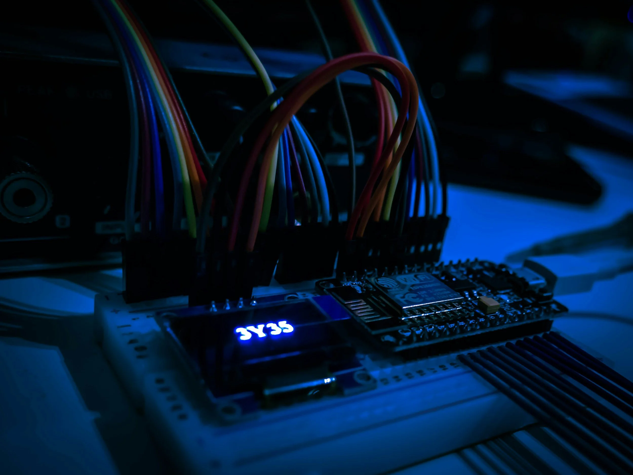 Close-up of an electronic circuit board with multicolored wires connected to it, illuminated by blue LED lights.