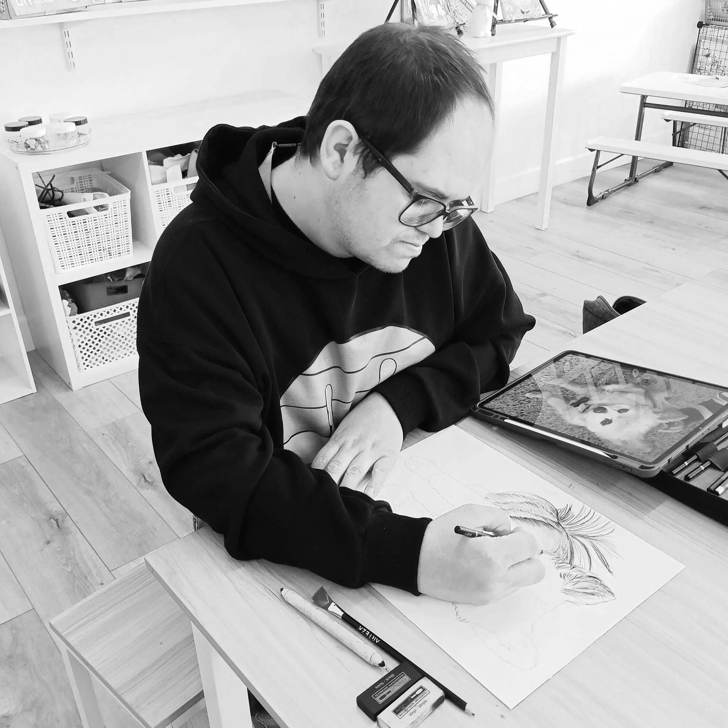 A man with glasses drawing on a paper with colored pencils on a wooden table.