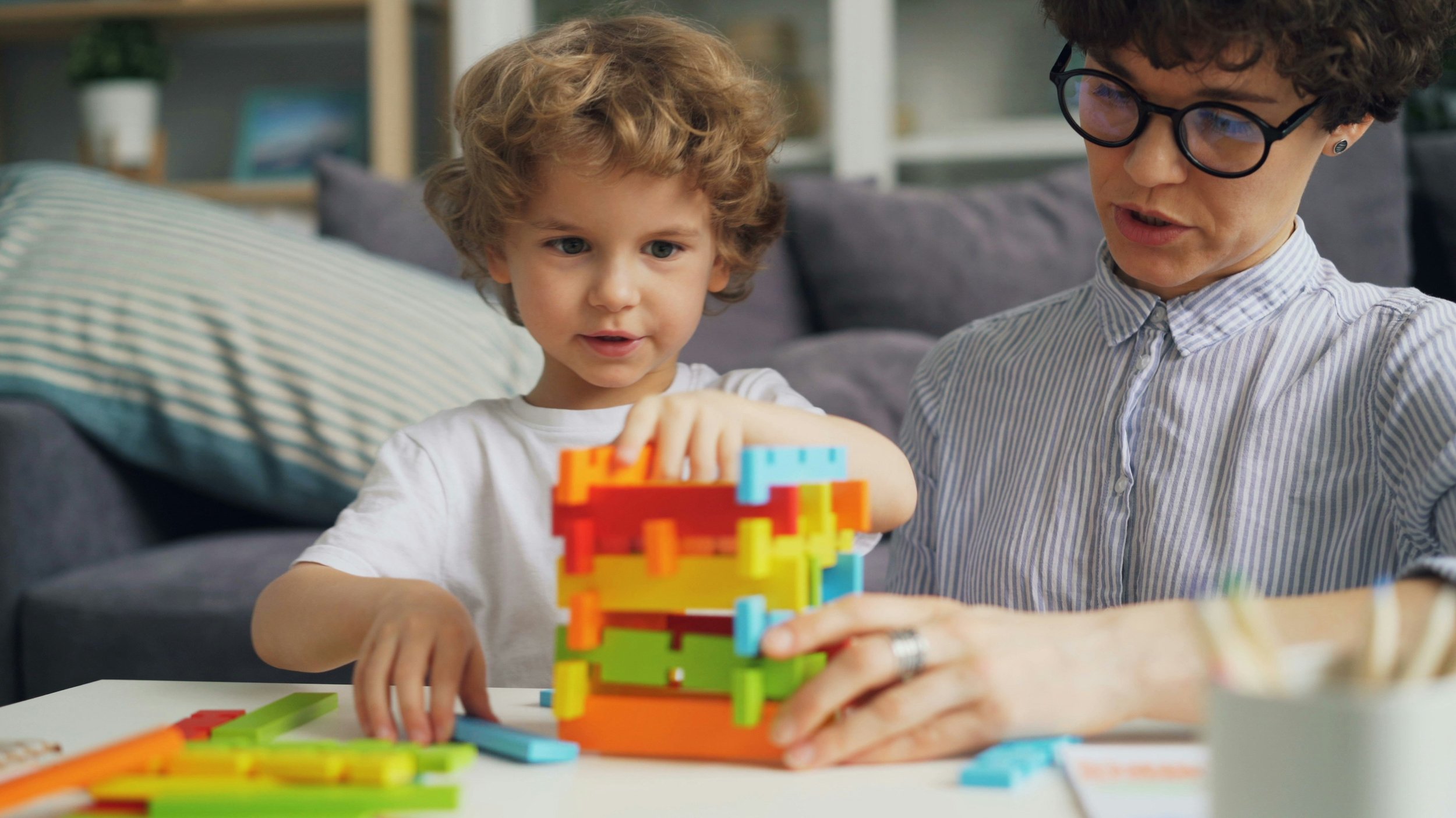 A young boy and woman playing with colorful building blocks on a table in a living room.