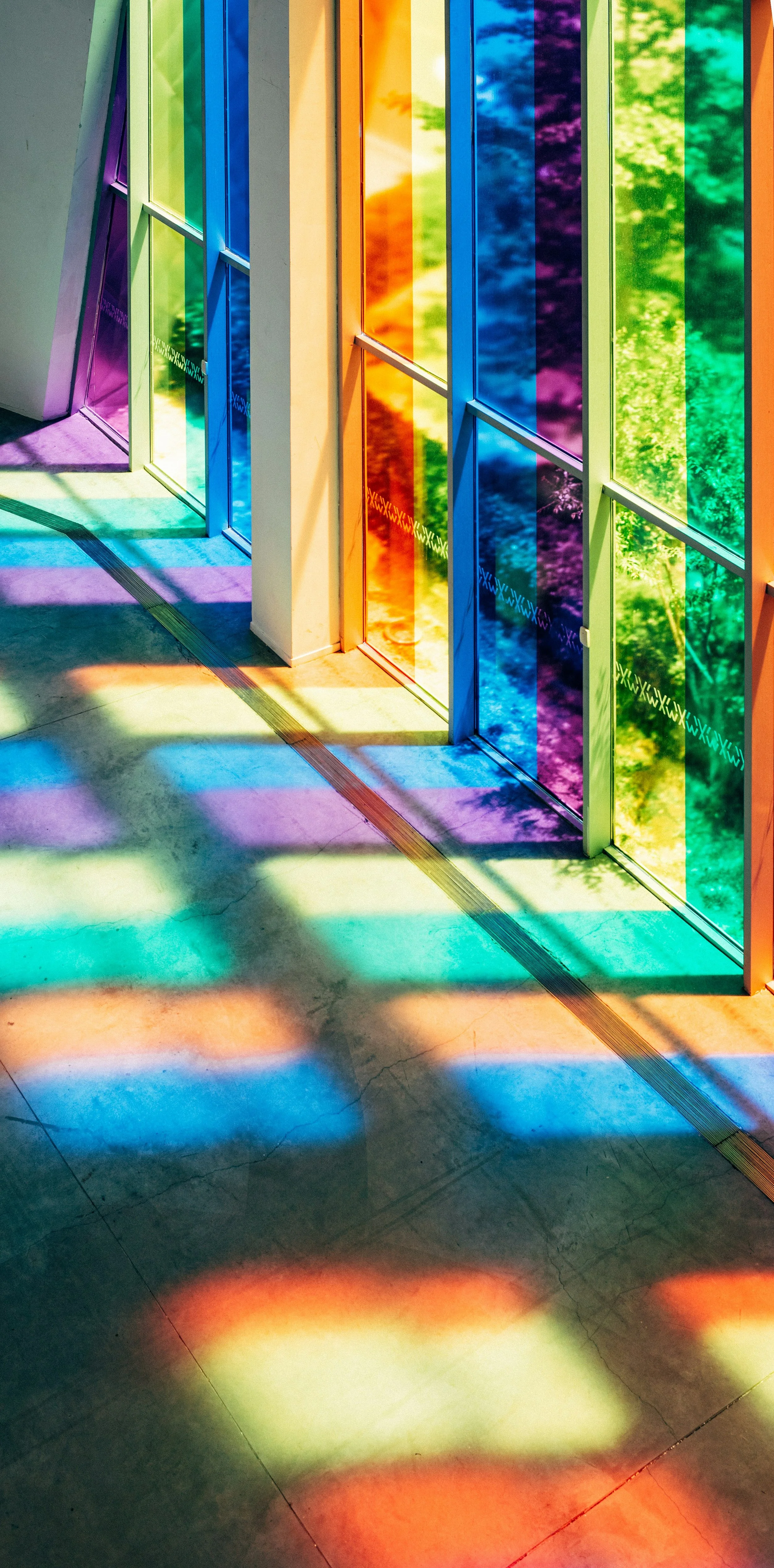 Colorful glass panels on a window casting rainbow shadows on the floor.