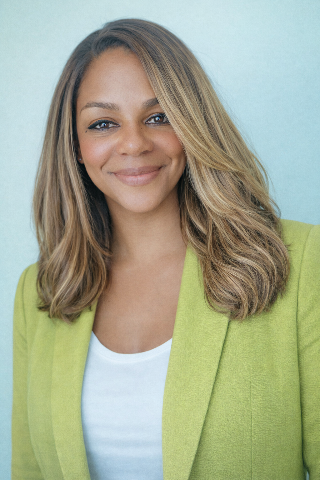 A woman with light brown hair and light skin, wearing a light green blazer over a white top, smiling at the camera against a light blue background.