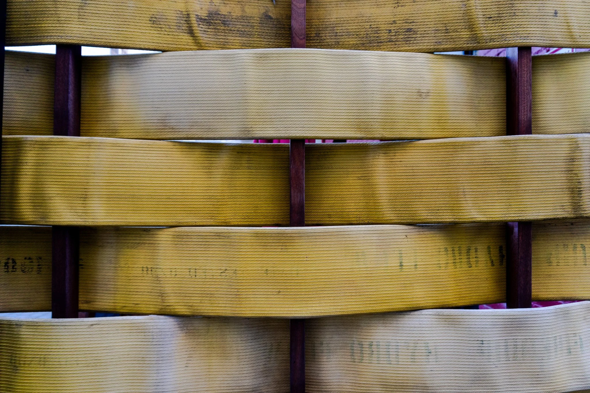 Close-up of yellowish-brown woven wood slats arranged horizontally with purple vertical supports in between.