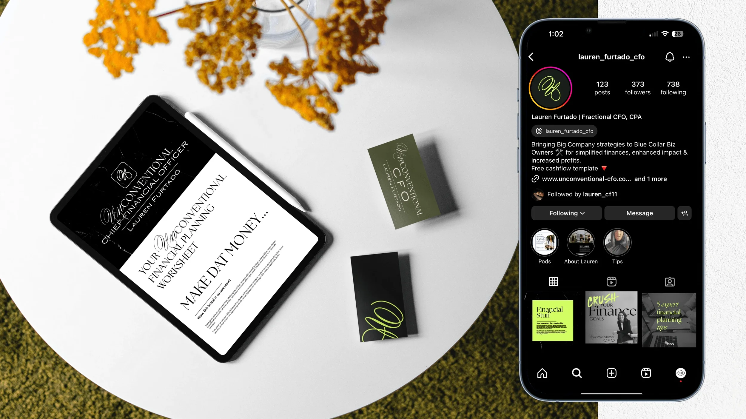A white table with a tablet displaying a worksheet titled 'Your Financial & Planning Worksheet Make Data.' Next to the tablet are business cards and dried yellow flowers. A smartphone shows an Instagram profile for Lauren Furtado, a fractional CFO and CPA, with posts related to finance and financial tips.