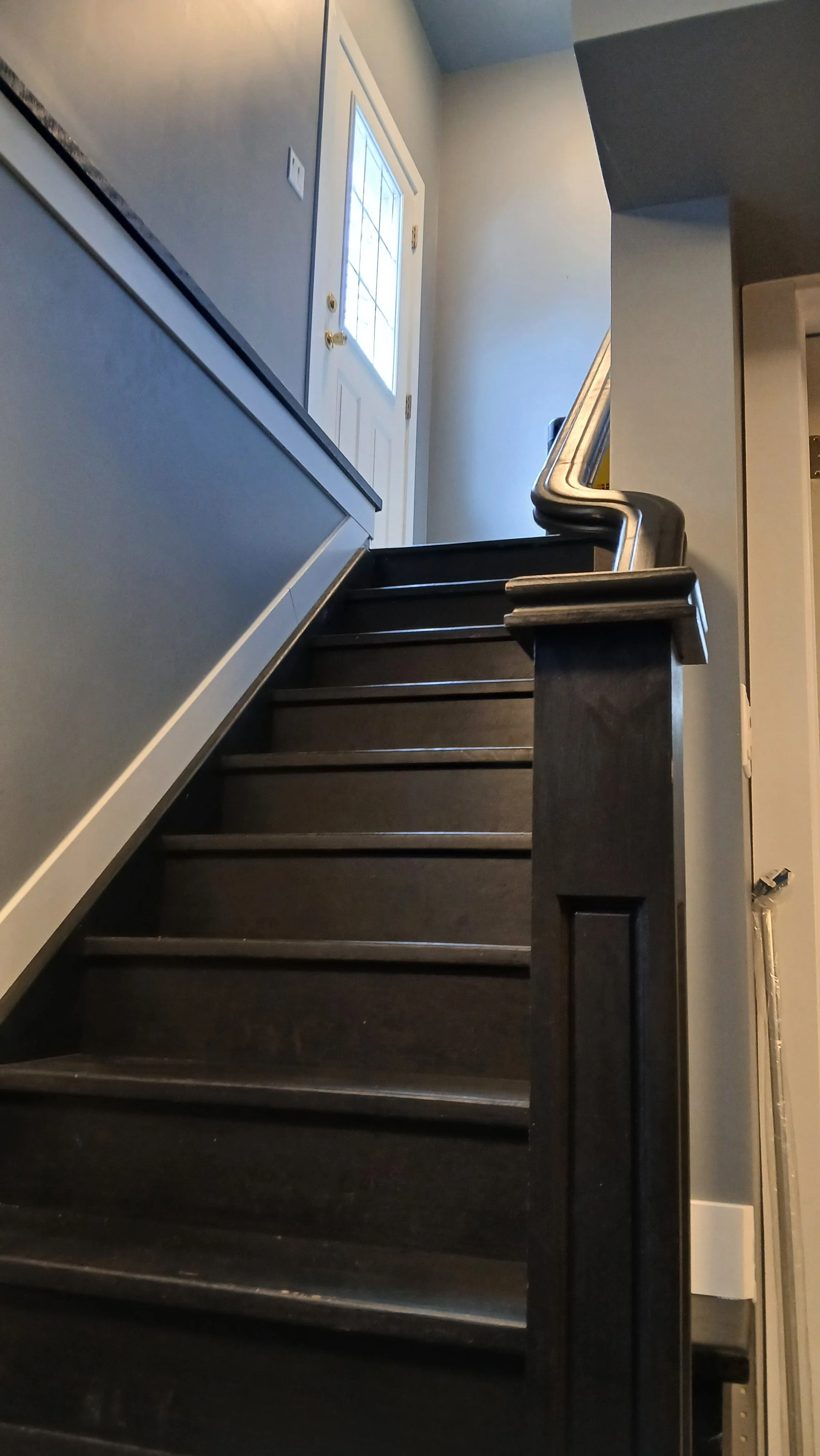 Dark wooden indoor staircase with a handrail, leading up to a white door with glass panels, in a home's interior.