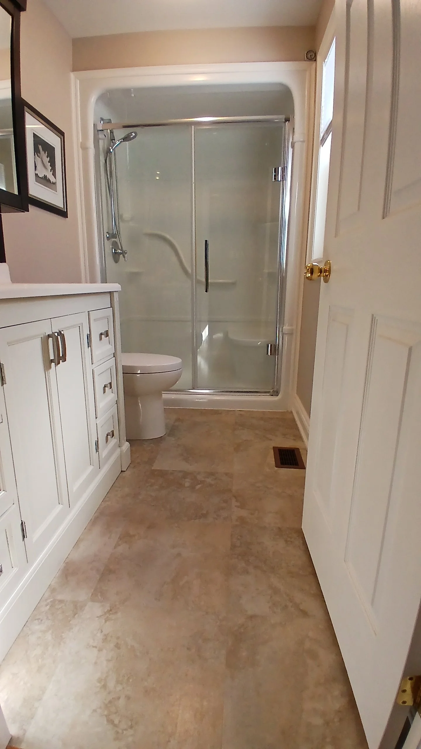 Bathroom with a glass shower enclosure, toilet, and white vanity cabinet, beige walls, and tiled floor.