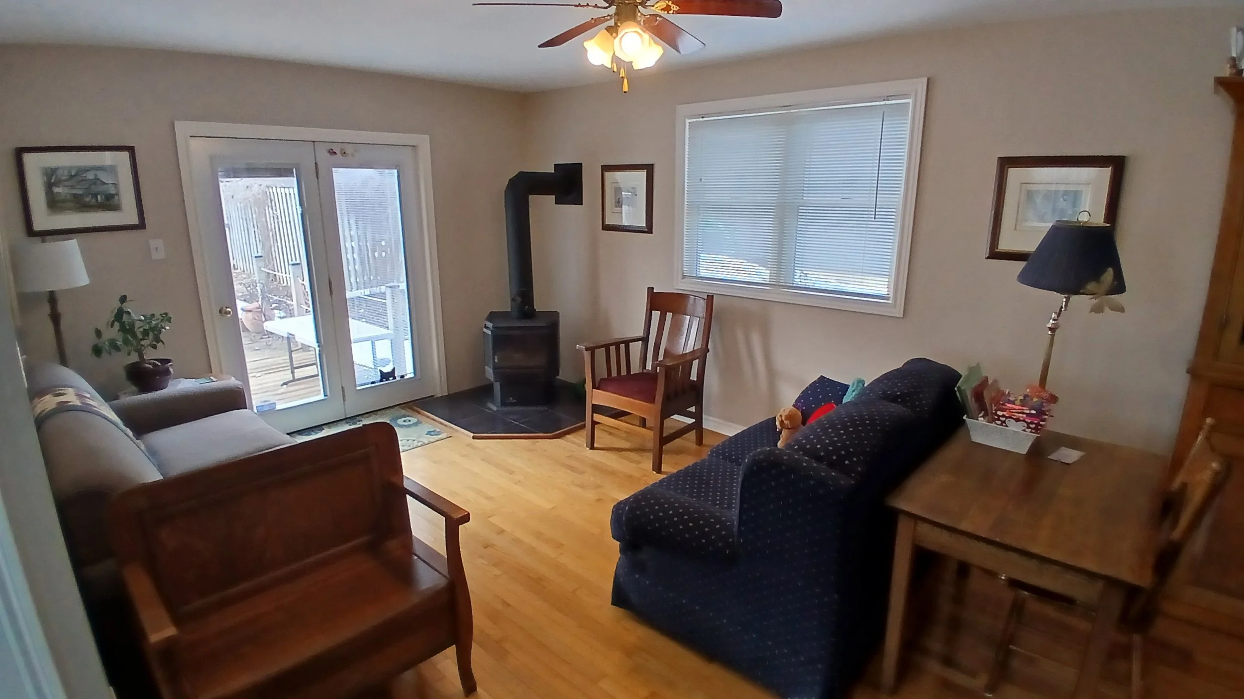 Living room with a ceiling fan, wooden furniture, a patterned sofa, a reclining chair, large window with blinds, and a glass sliding door leading outside.