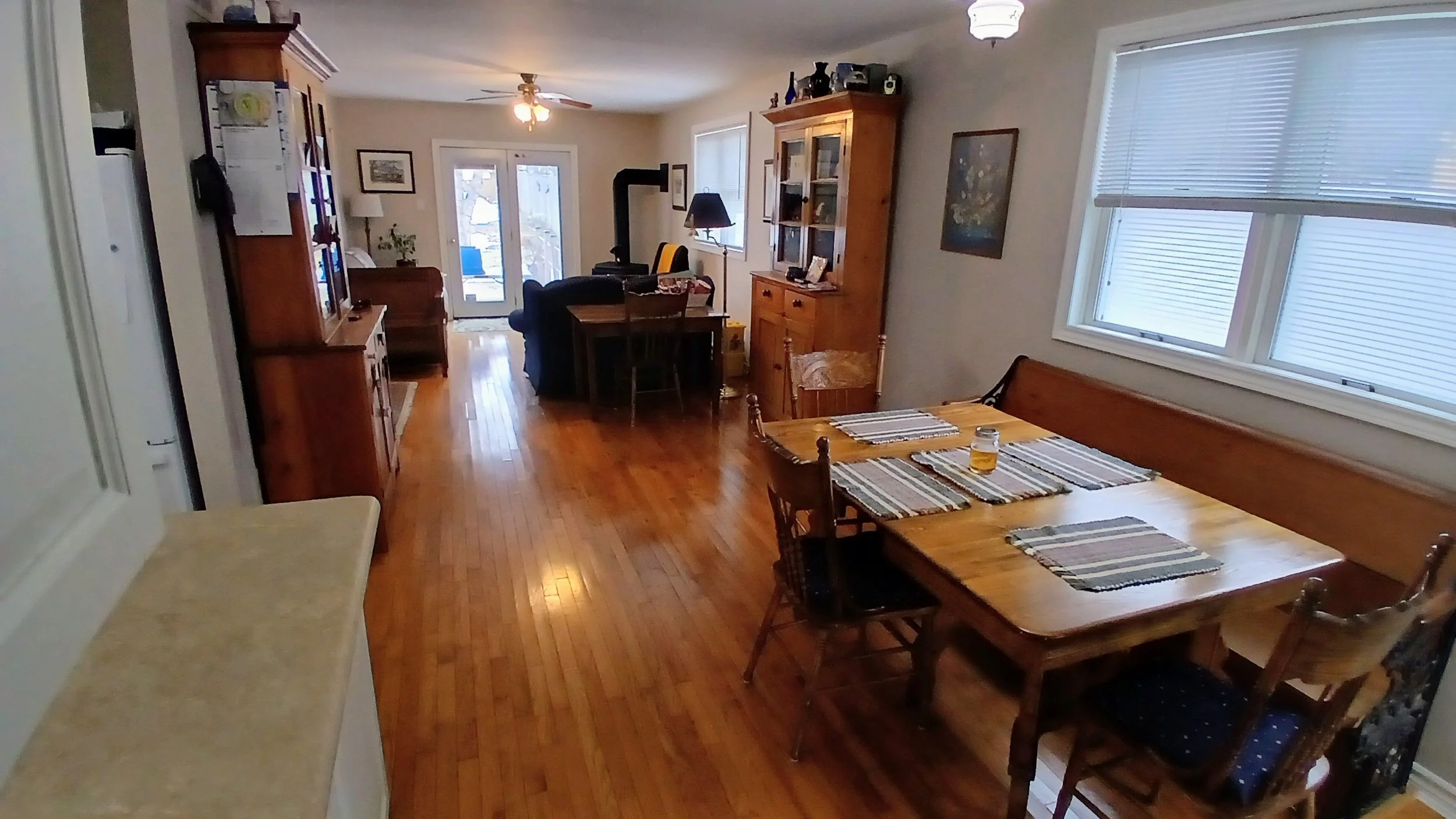 Living and dining area with hardwood floors, a wooden dining table with striped placemats, a window with blinds, a wooden cabinet, and a sliding glass door leading outside.