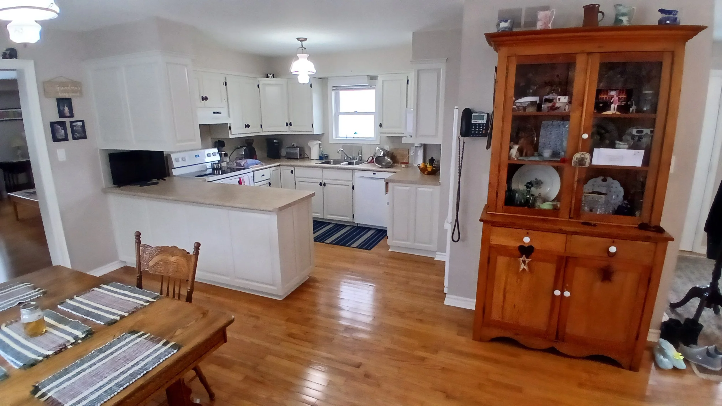 A cozy kitchen with white cabinets, a window above the sink, and a wooden dining table with striped placemats.