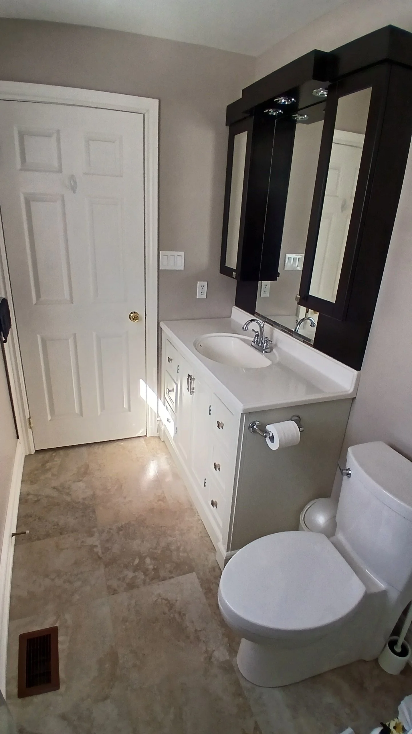 A small bathroom with a white vanity, black medicine cabinet, mirror, toilet, and beige tile floor.