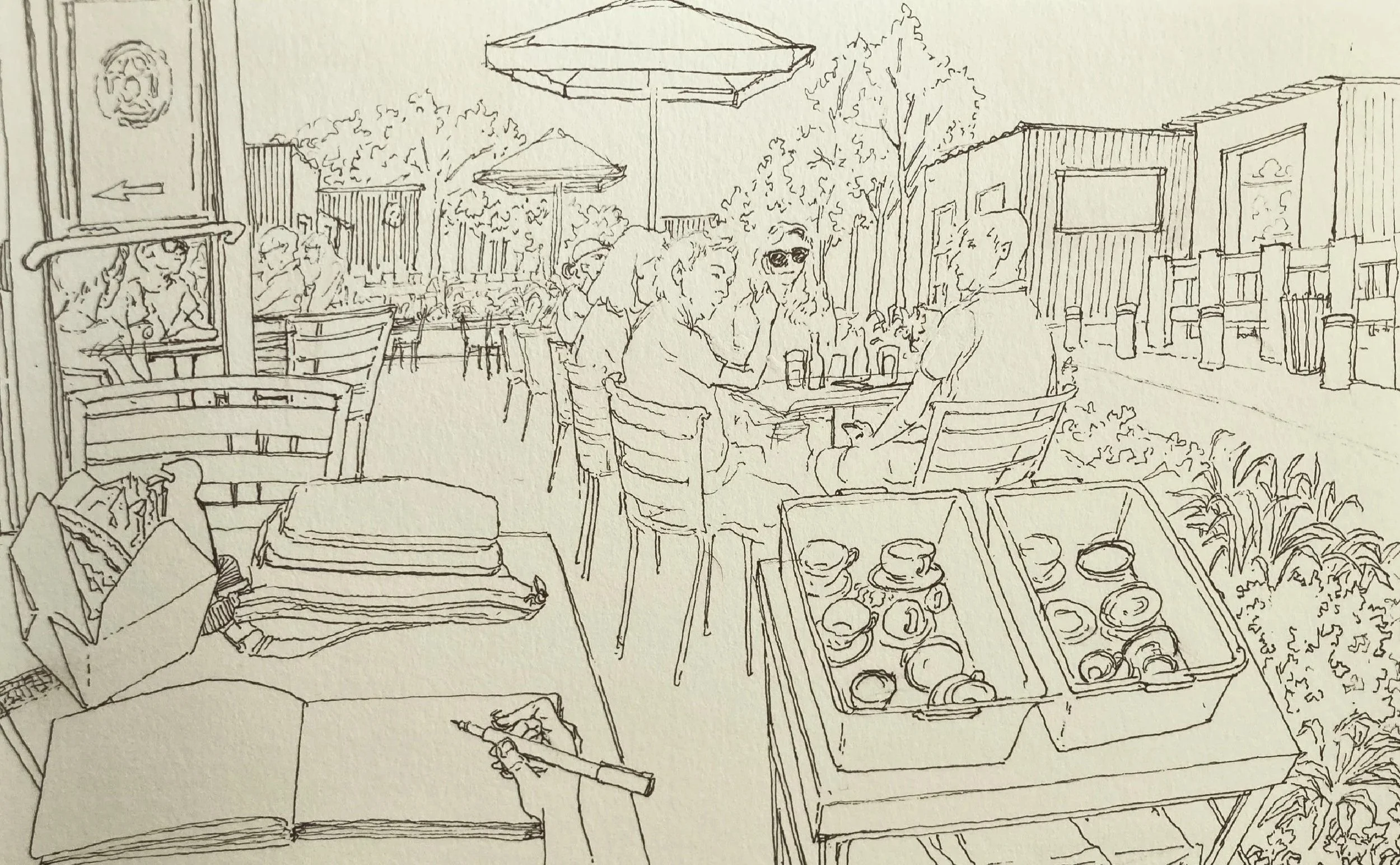 Line drawing of an outdoor café with people sitting at tables, umbrellas, and a food stand with baked goods in the foreground.