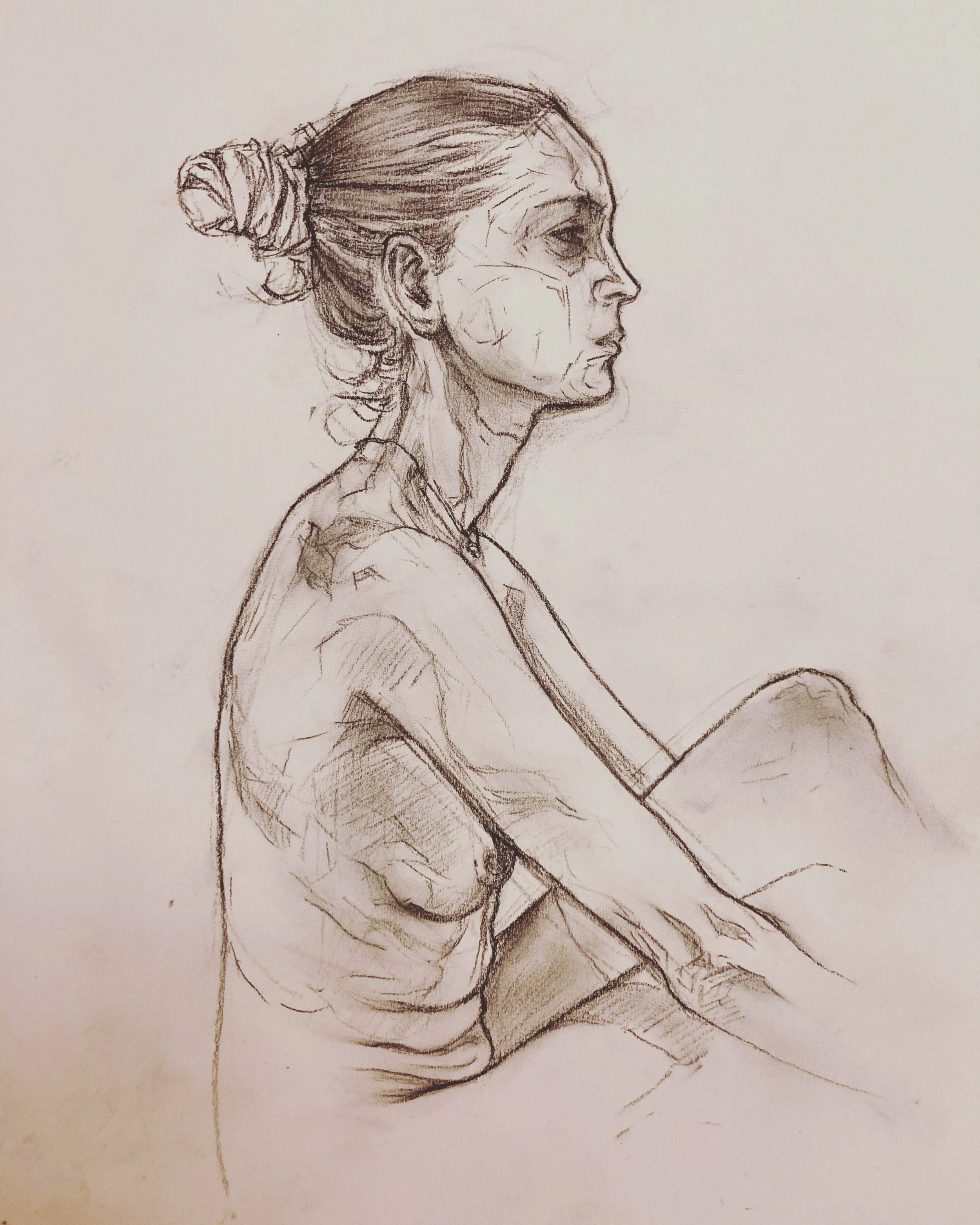 A detailed pencil sketch of a woman in profile with her hair tied up in a bun, wearing a short-sleeved shirt, sitting with her arms resting on her knees.