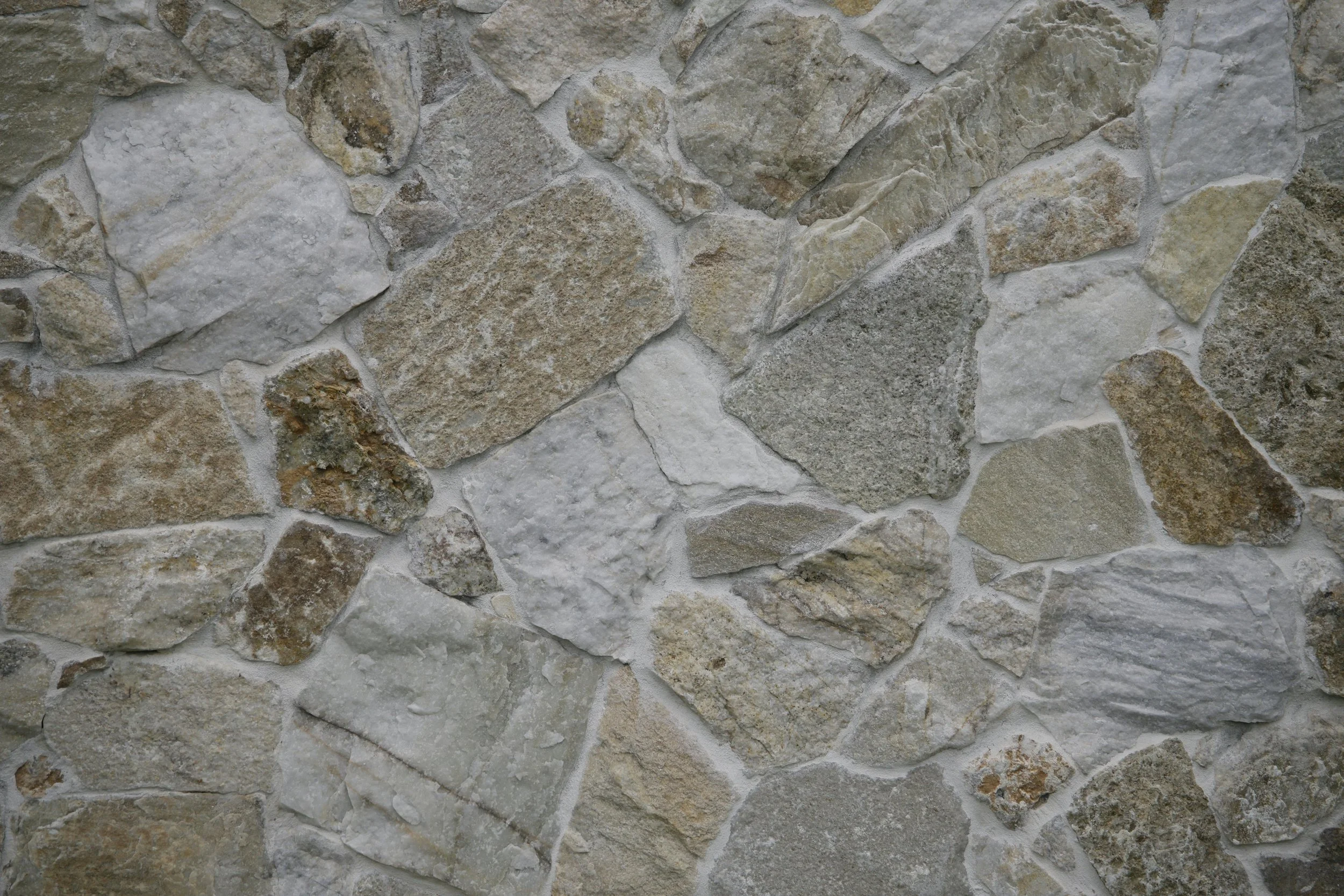 Close-up view of a textured stone wall with irregularly shaped stones in shades of beige, gray, and brown held together with mortar.