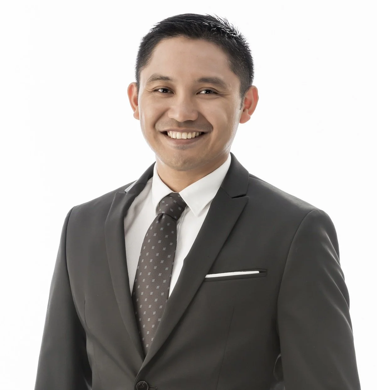 A smiling man in a black suit, white shirt, and patterned tie, standing against a white background.