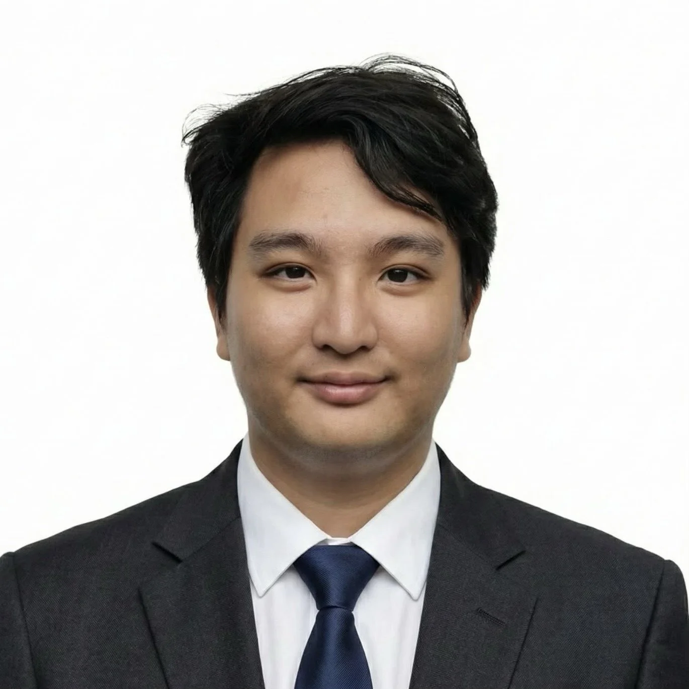 Portrait of a young man with dark hair, wearing a black suit, white collared shirt, and dark blue tie, against a plain white background.