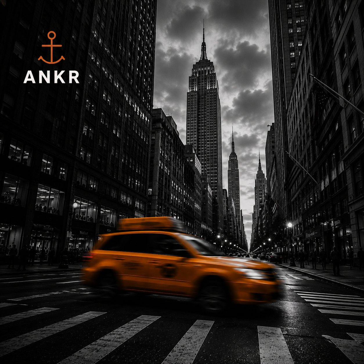 Black and white city street scene with tall skyscrapers, the Empire State Building in the background, and a blurred yellow taxi cab in motion at a crosswalk.