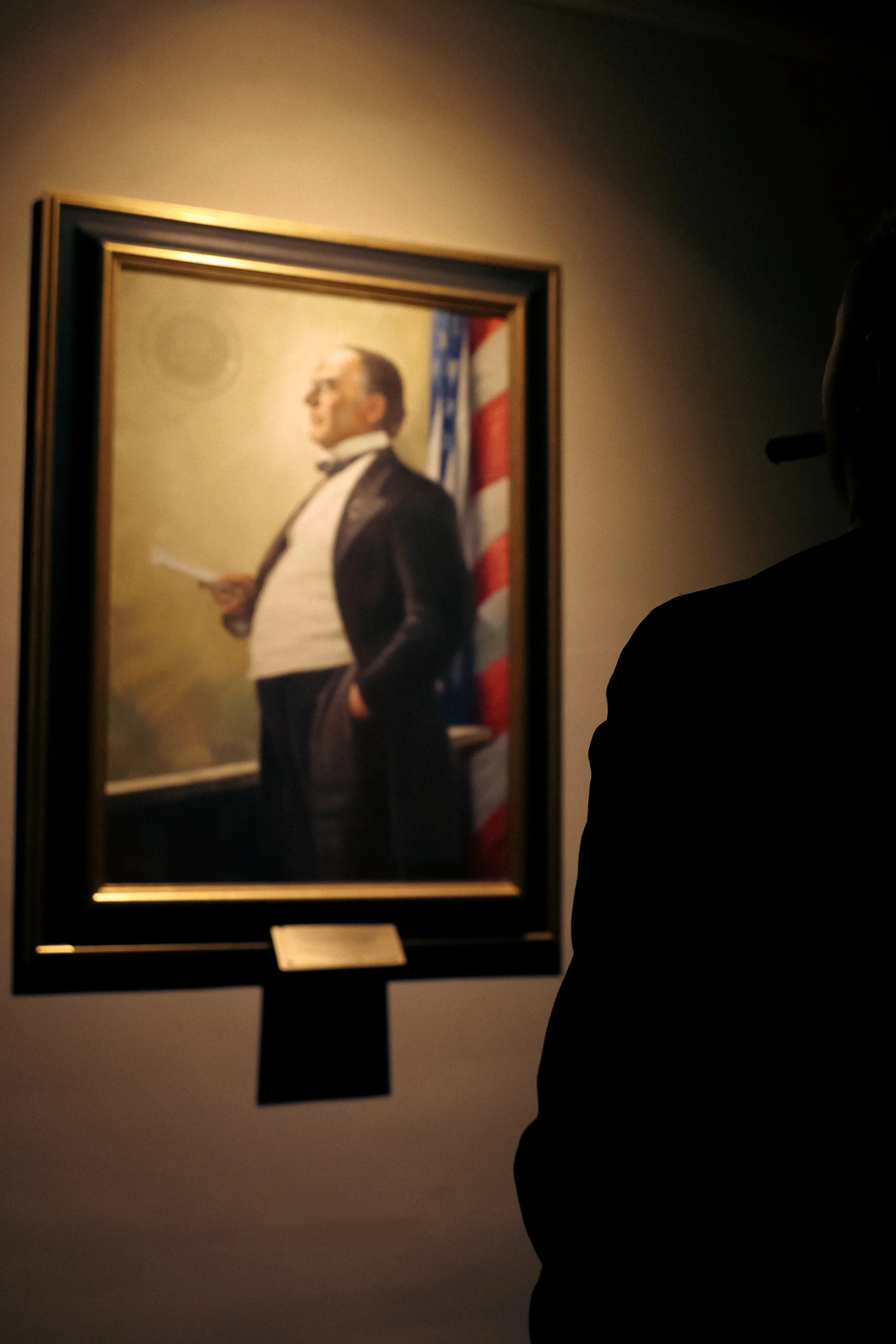 A person viewing a framed portrait of Abraham Lincoln displayed in a dimly lit museum or gallery.
