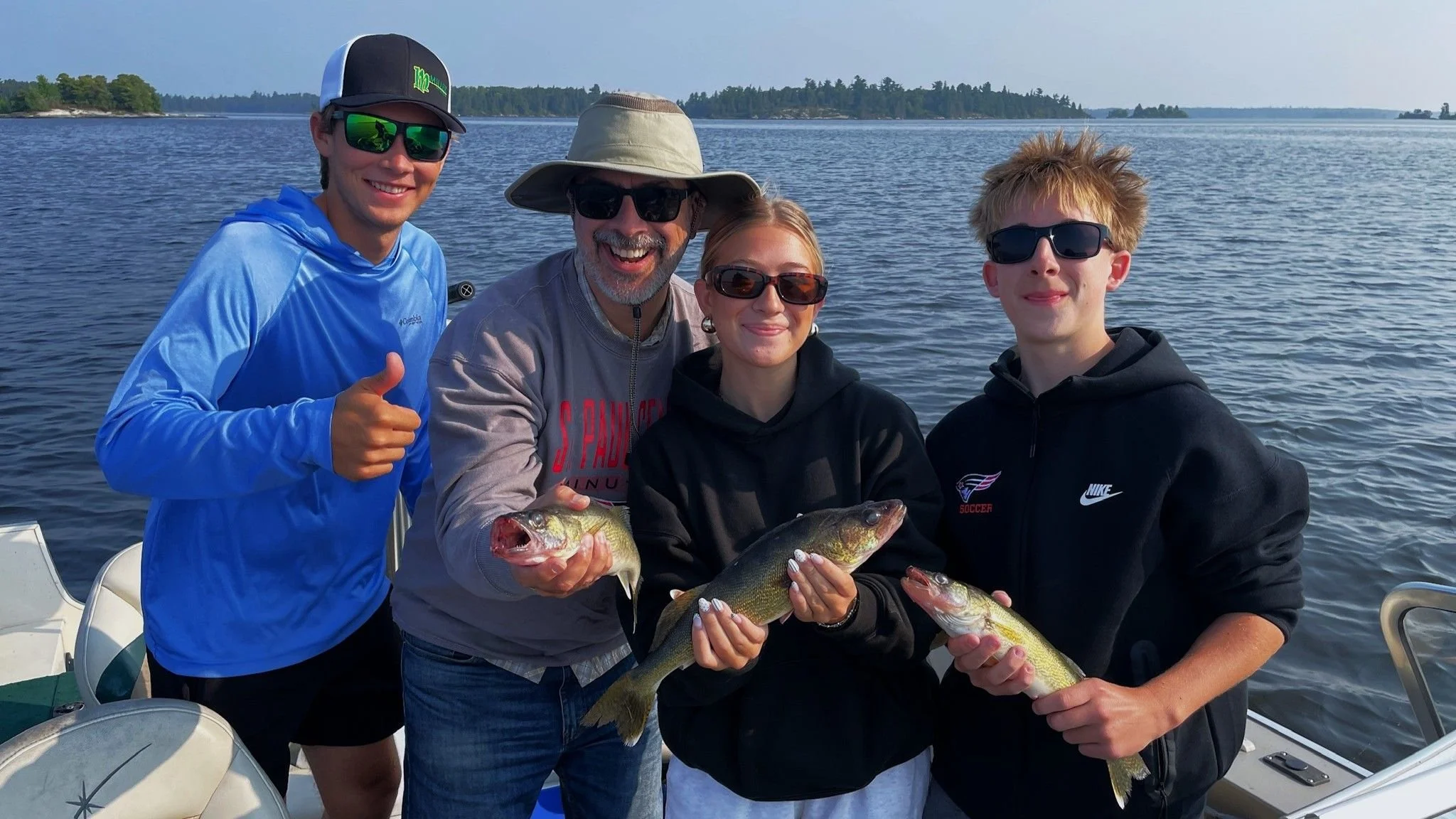 Group of five people on a boat holding fish they caught, with water and distant land in the background.