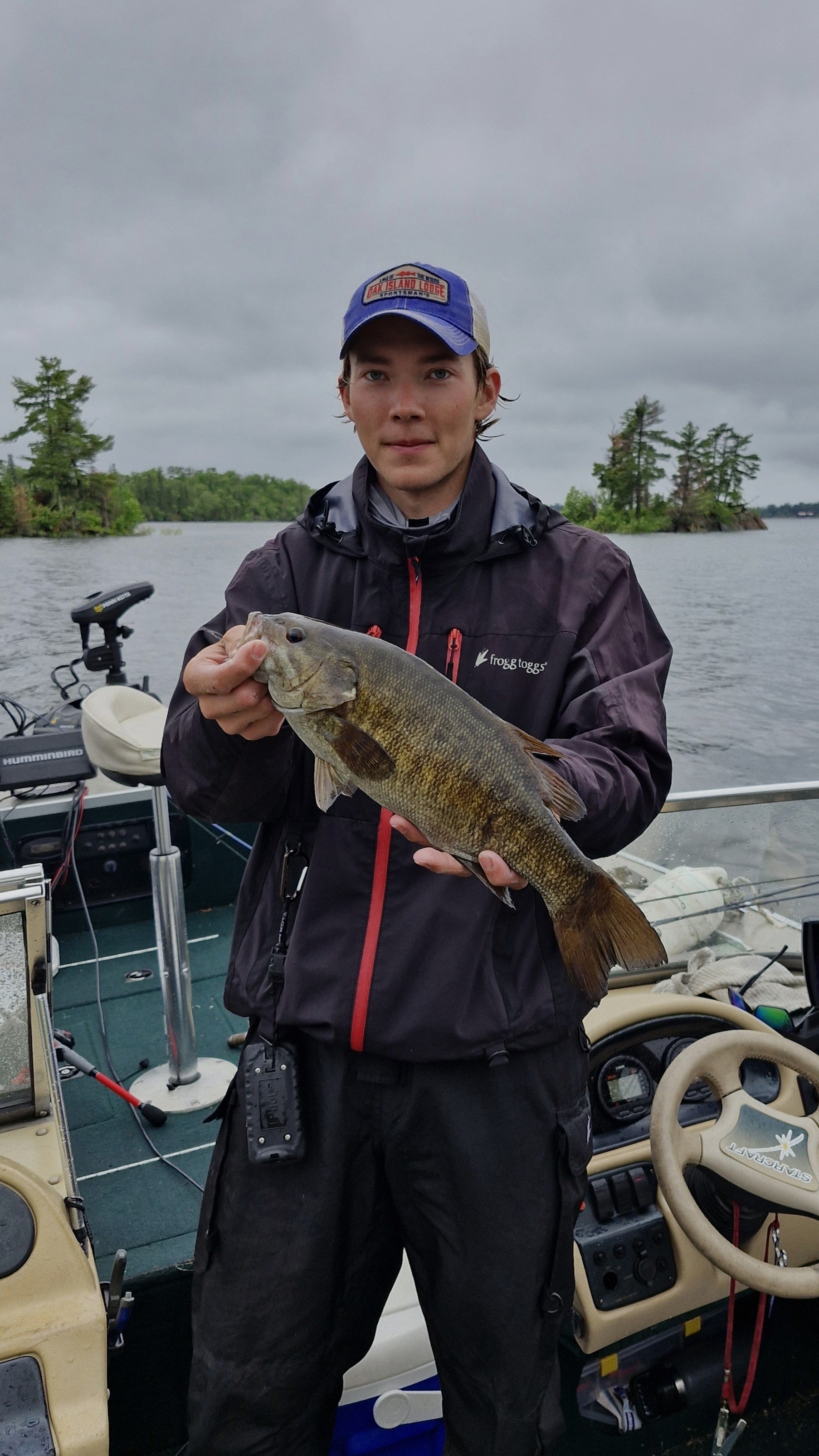 Guide Eric holding a large fish on a boat during a cloudy day, with water and trees in the background.