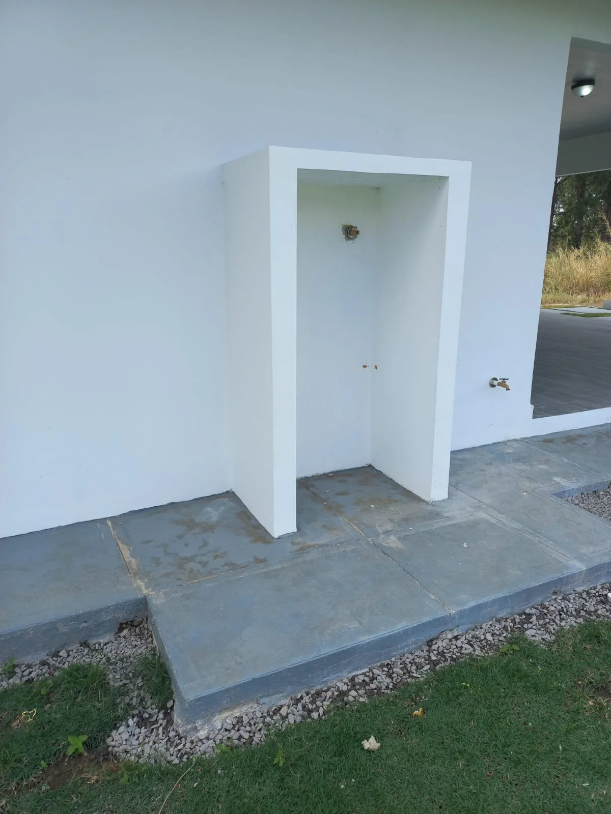 Empty outdoor laundry area with a white wall, ground pipe fittings, and a concrete step leading to a grassy area.